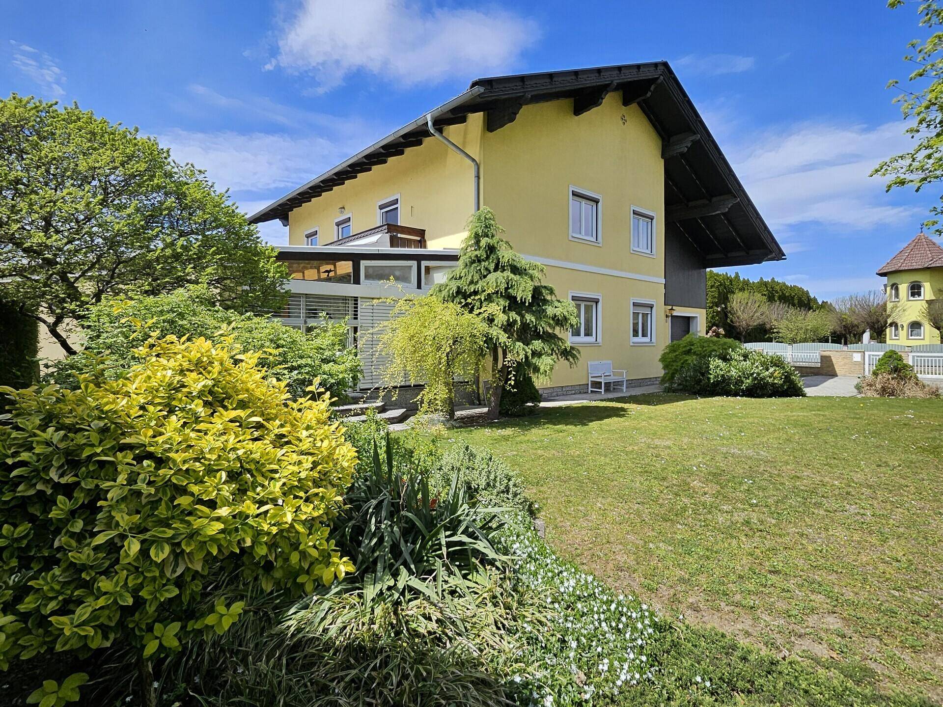 Gepflegter Garten mit vielfältigen Pflanzen und Blick auf die gelbe Hausfassade.