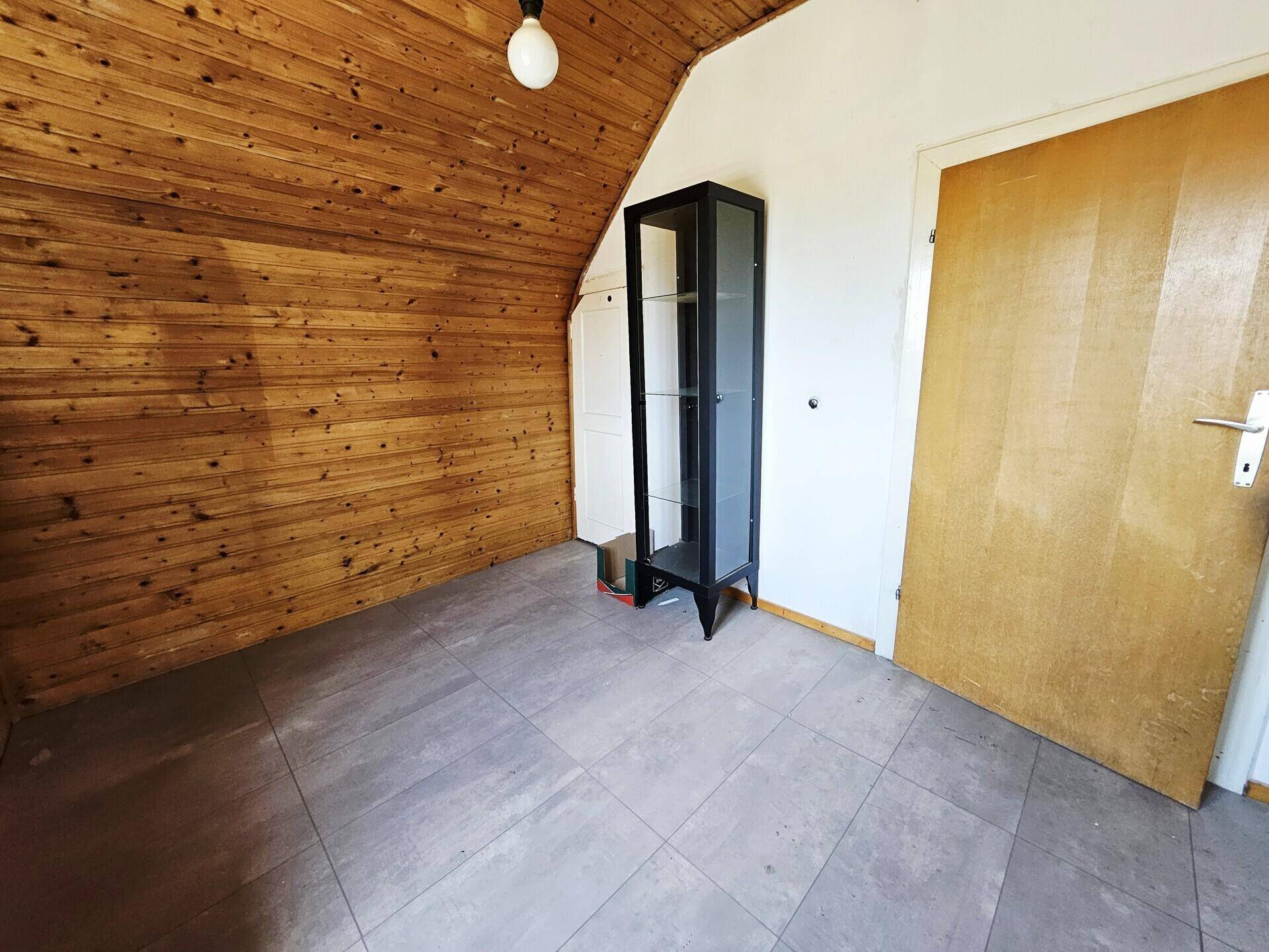 Dachzimmer mit Holzvertäfelung, Fliesenboden und einer einfachen Einrichtung.
