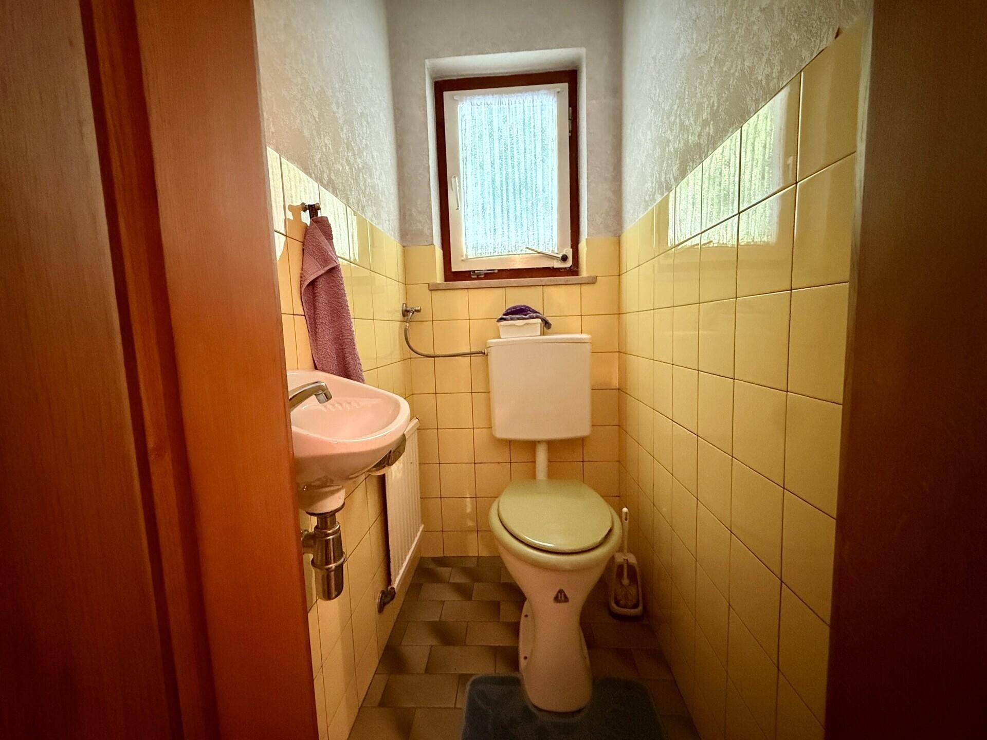 Kleines Gäste-WC mit gelben Fliesen, Waschbecken und Fenster, funktional eingerichtet.
