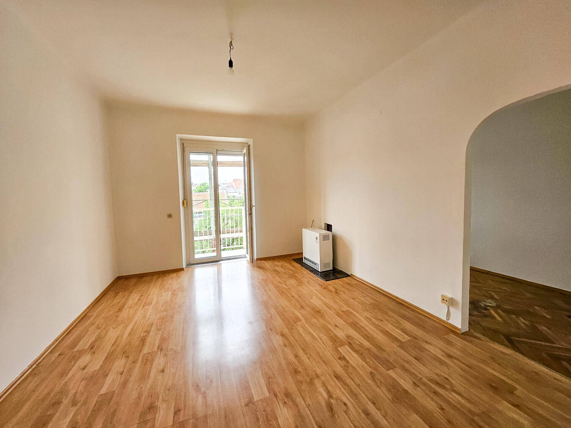 Helles Zimmer mit Holzboden und Zugang zu einem Balkon, ideal für entspannte Stunden.