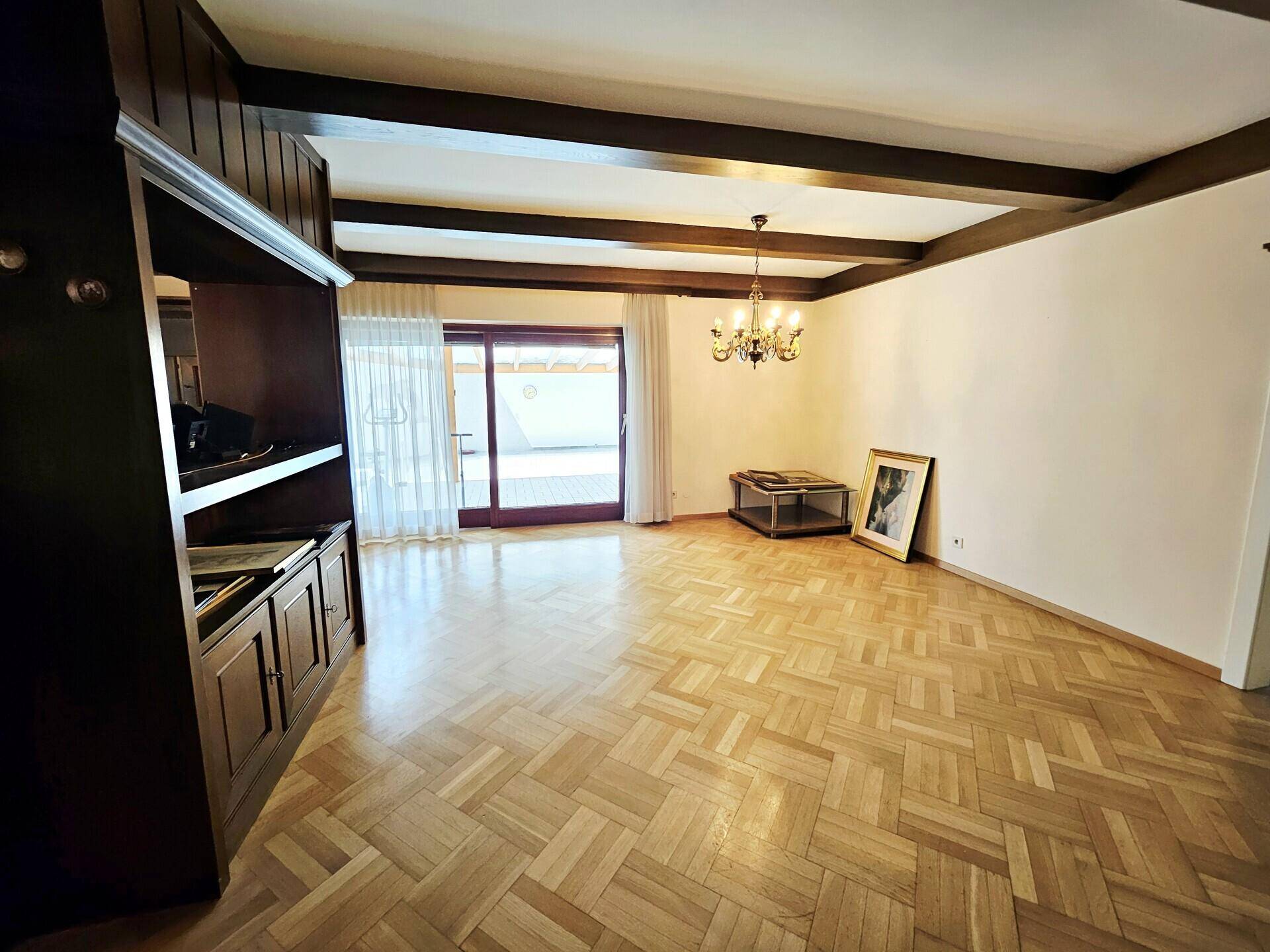 Geräumiges Wohnzimmer mit Parkettboden, Holzbalkendecke und Zugang zur Terrasse.