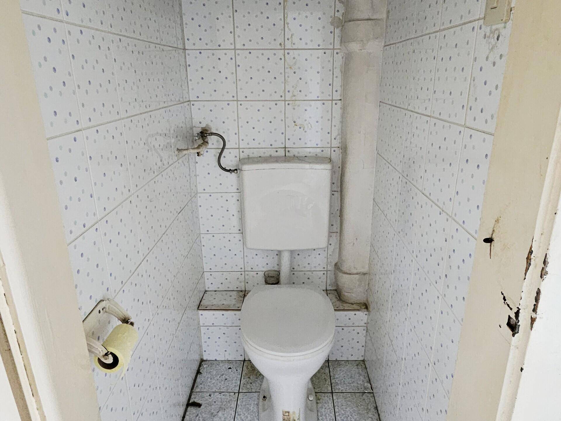 Kleines WC mit weißen Fliesen und einem einfachen Stand-WC.