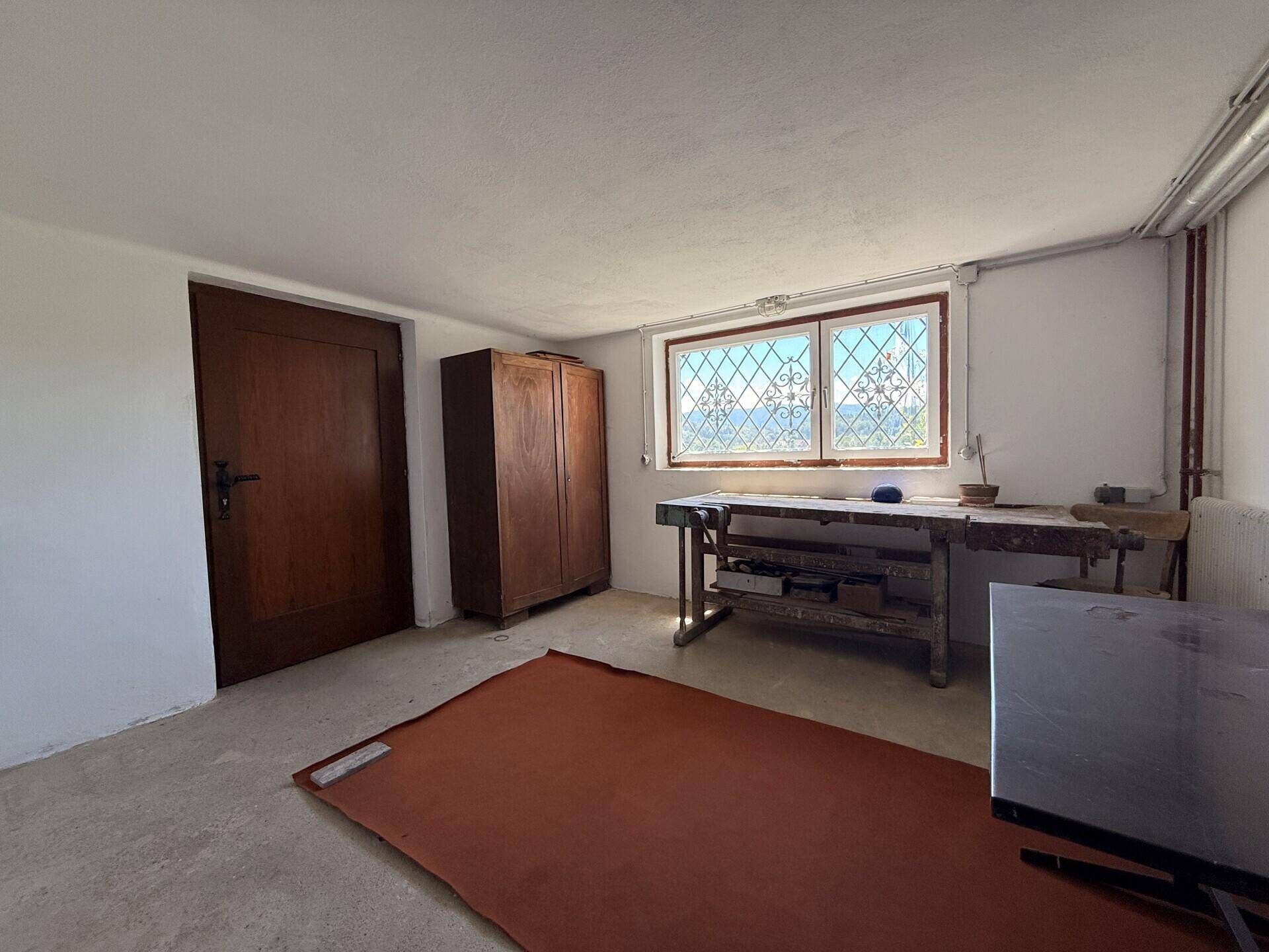 Werkstatt im Untergeschoss mit Werkbank, Schrank und Fenster, ideal für Heimwerker.