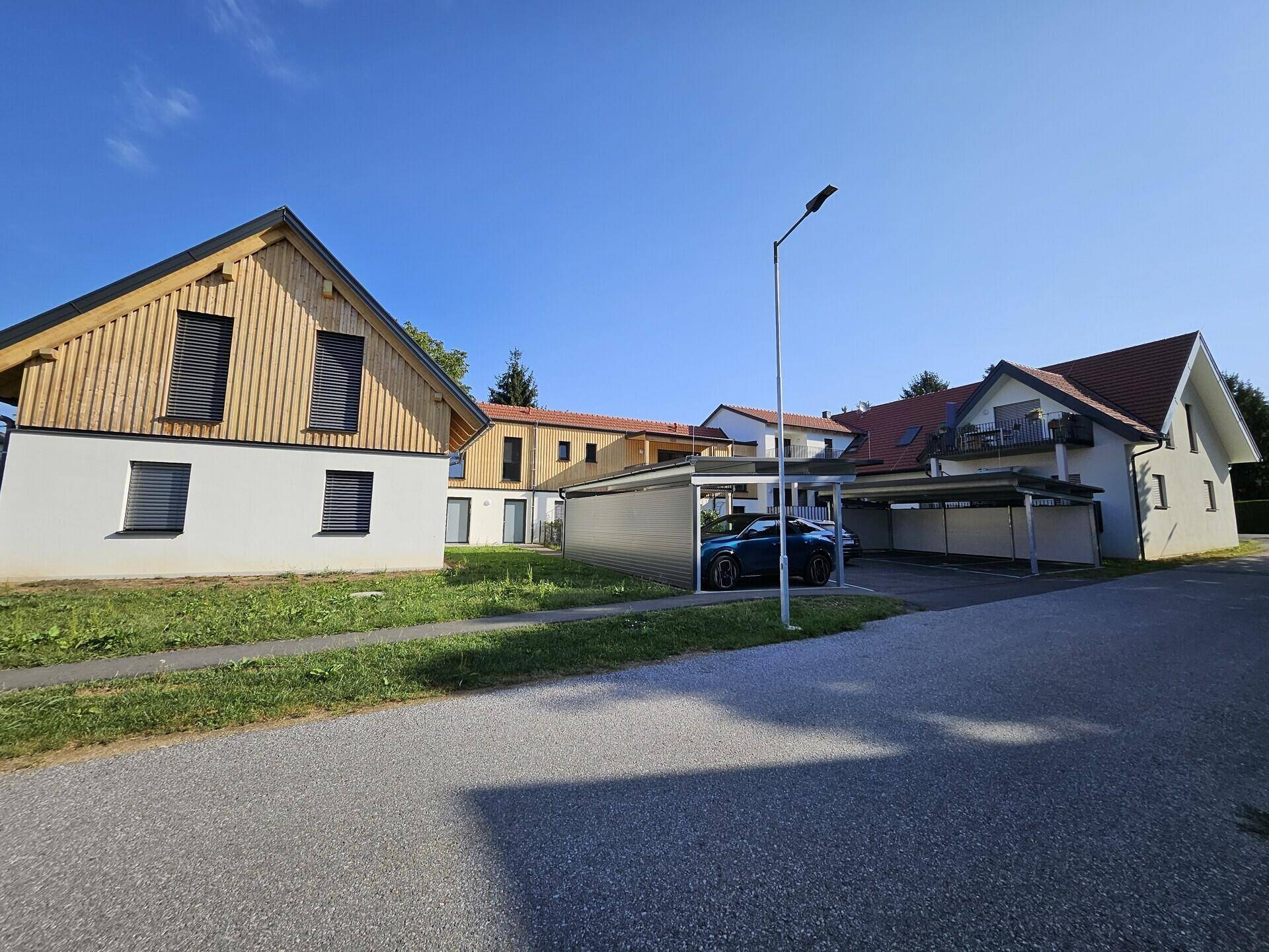 Ansicht der modernen Wohnanlage mit mehreren Gebäuden und überdachten Parkplätzen unter klarem Himmel.