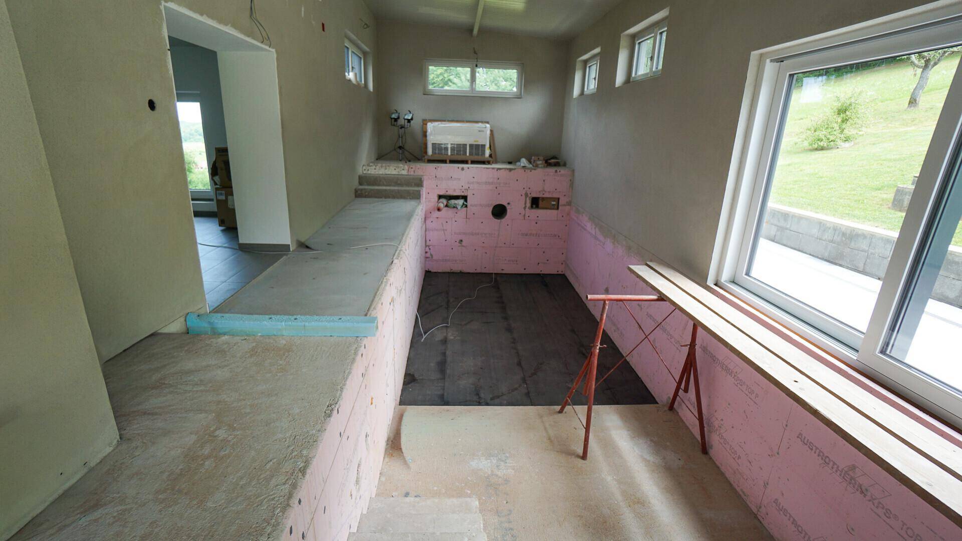 Innenraum im Rohbau, möglicherweise für einen Pool oder Wellnessbereich, mit großen Fenstern.