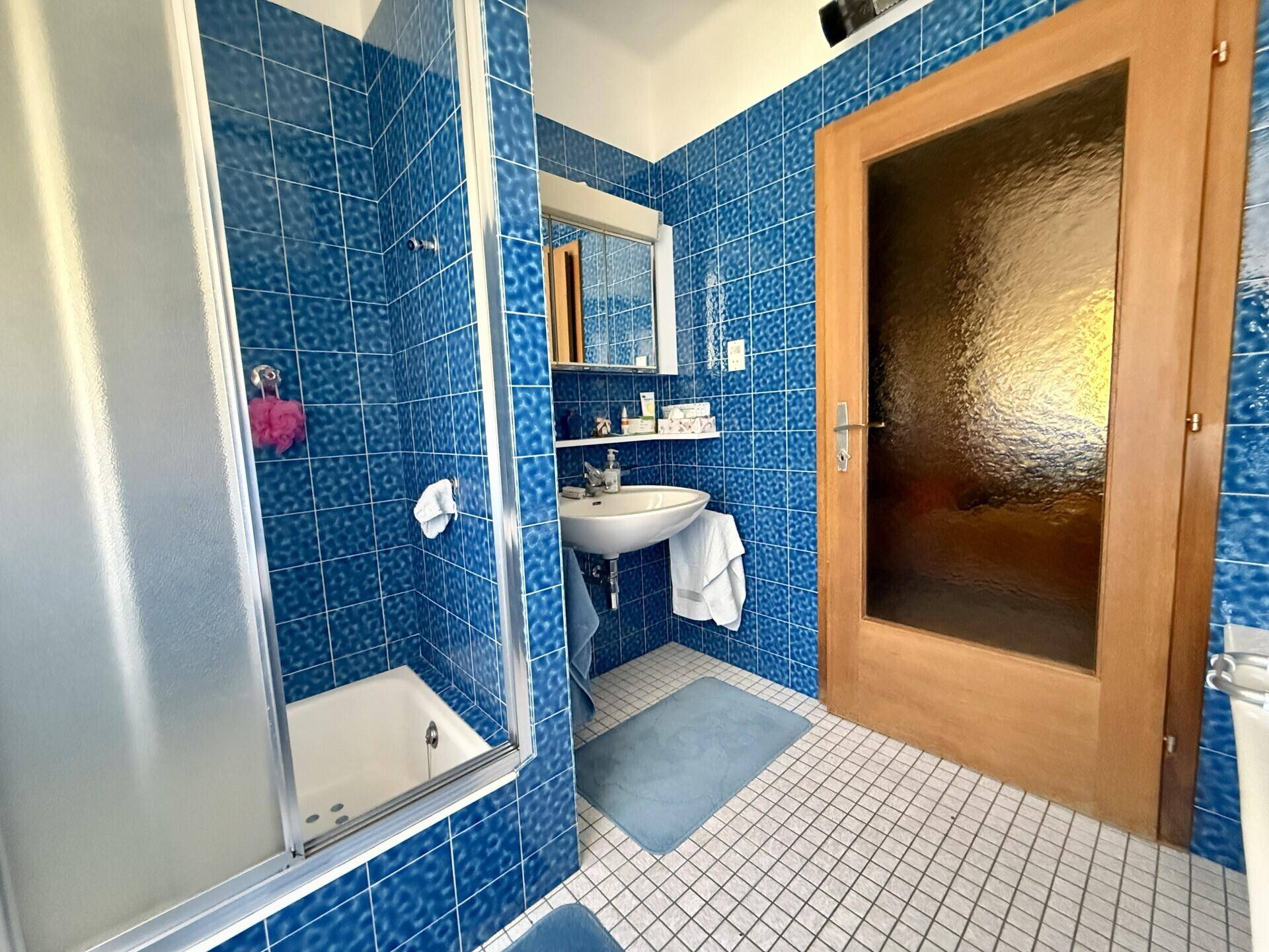 Badezimmer mit blauen Fliesen, Duschkabine und Waschbecken, im Stil der 80er Jahre.