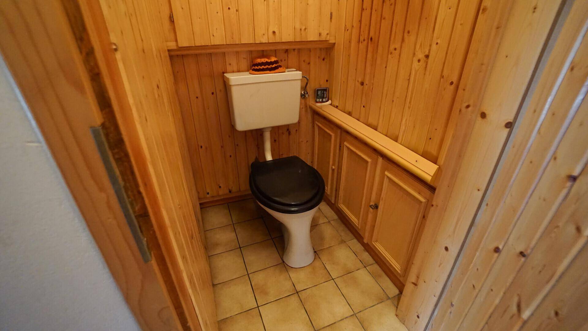 Kleines Gäste-WC mit Holzvertäfelung, Fliesenboden und einfacher Toilette.