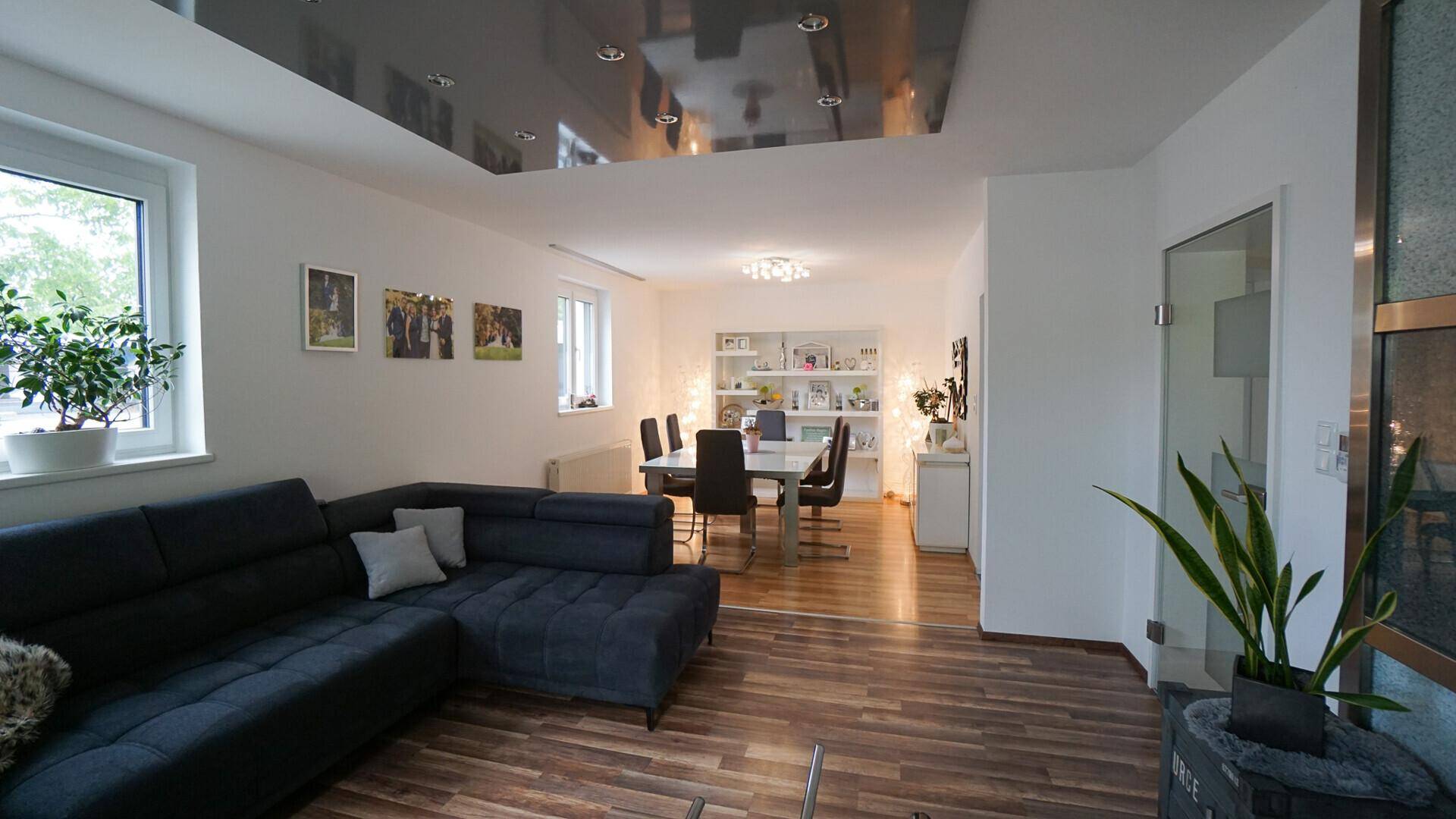 Geräumiger Wohn-Essbereich mit dunklem Sofa, Esstisch und moderner Deckenbeleuchtung.
