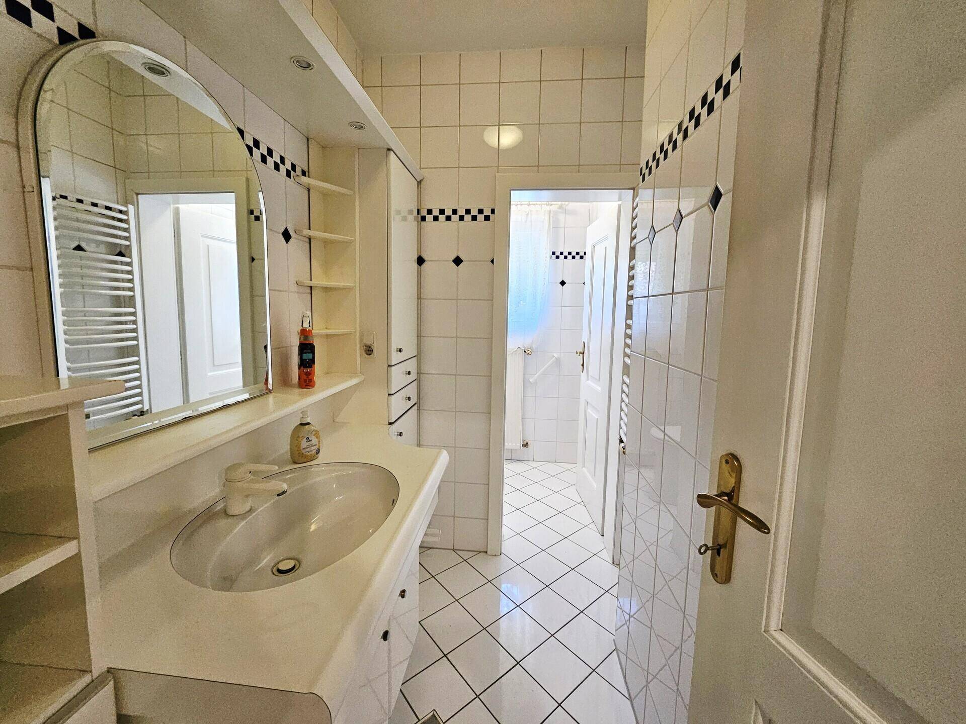 Badezimmer mit weiß gefliesten Wänden, Einzelwaschbecken und Spiegelschrank.