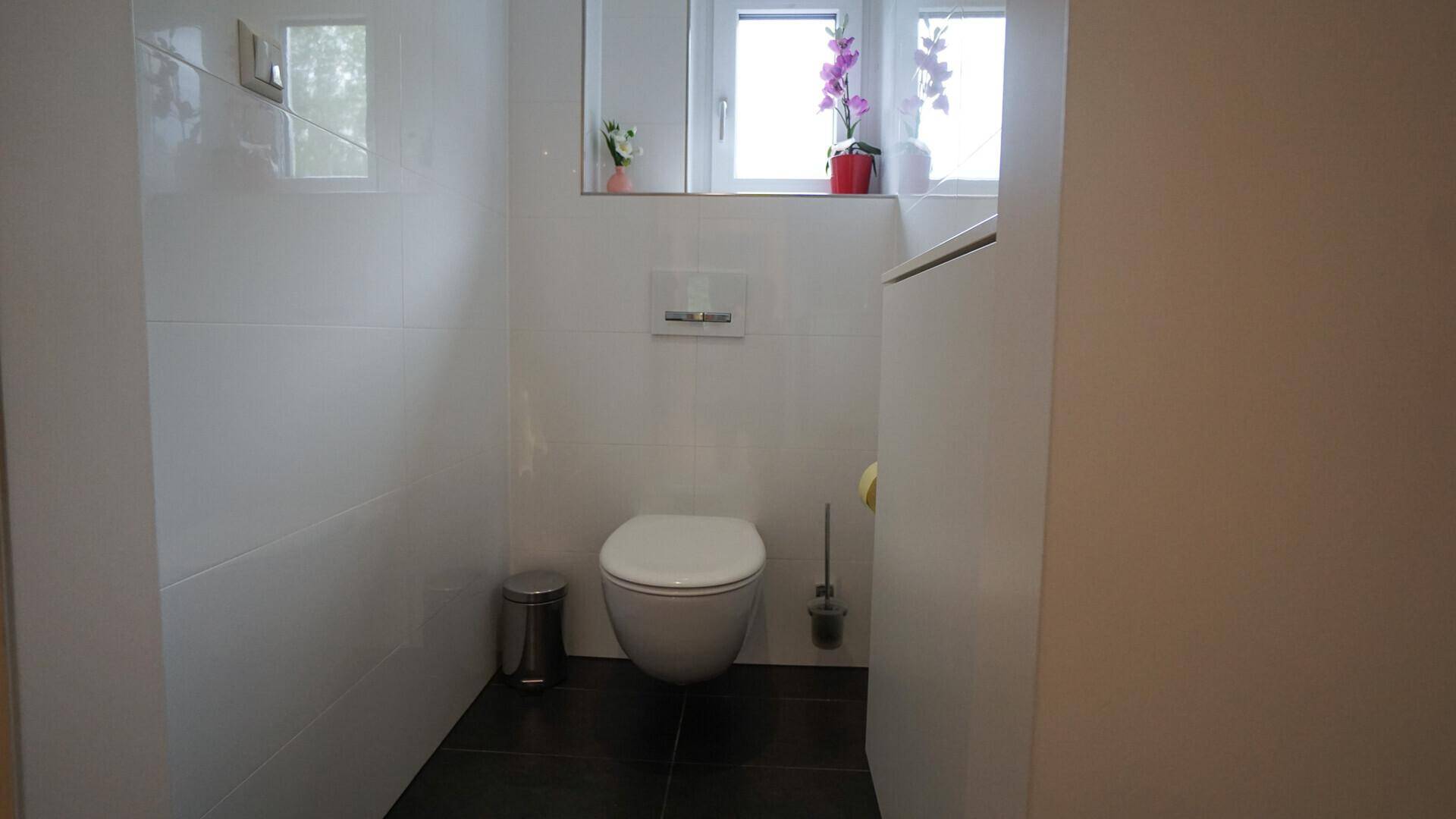 Modernes Gäste-WC mit wandhängender Toilette, weißen Fliesen und einem praktischen Fenster.