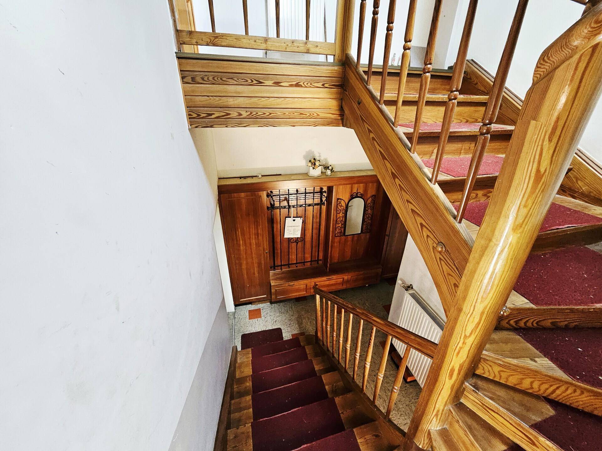 Blick von oben auf das Holztreppenhaus mit rotem Läufer und Garderobenbereich.