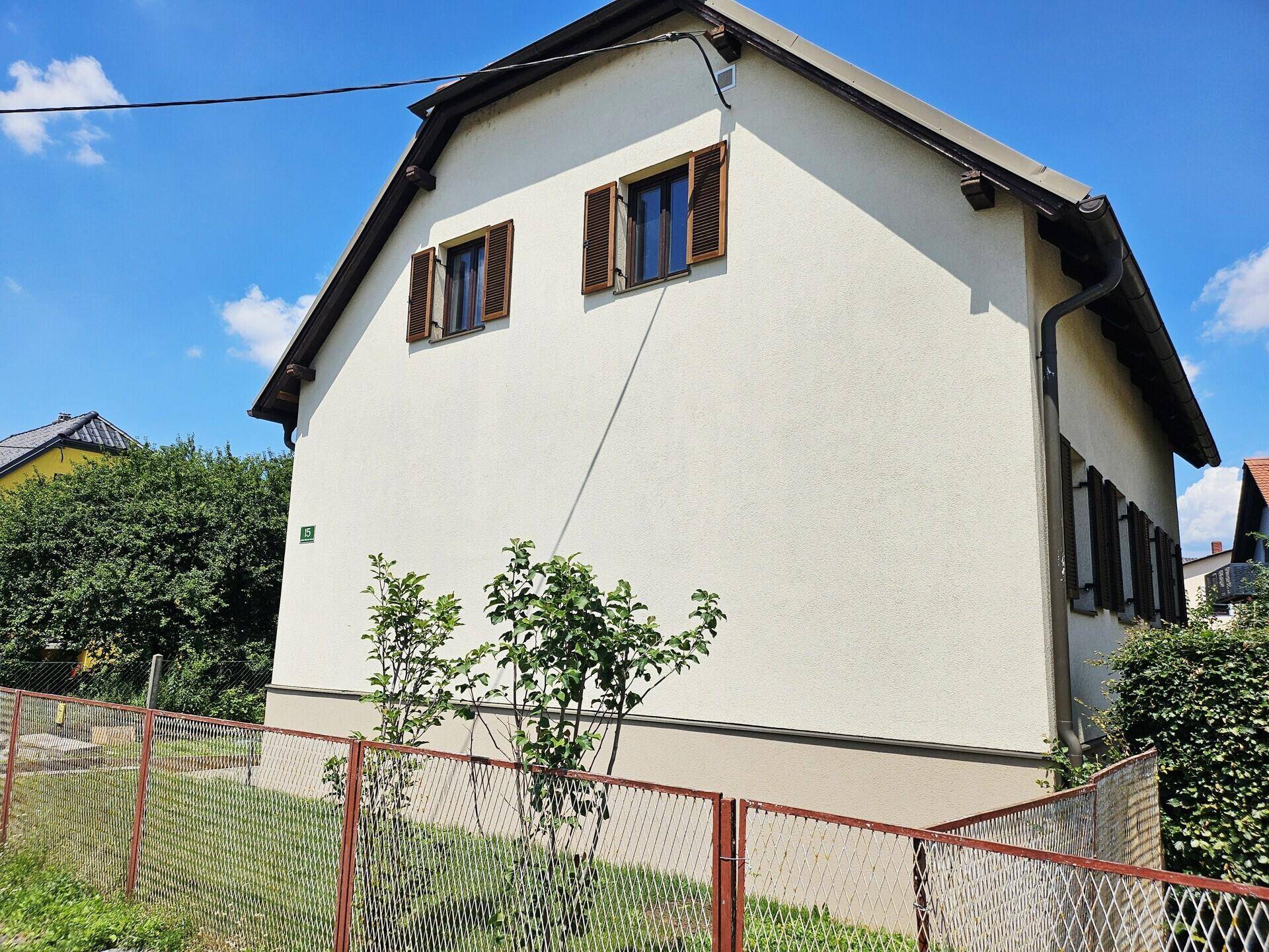 Seitenansicht des Wohnhauses mit Fenstern und braunen Fensterläden unter blauem Himmel.