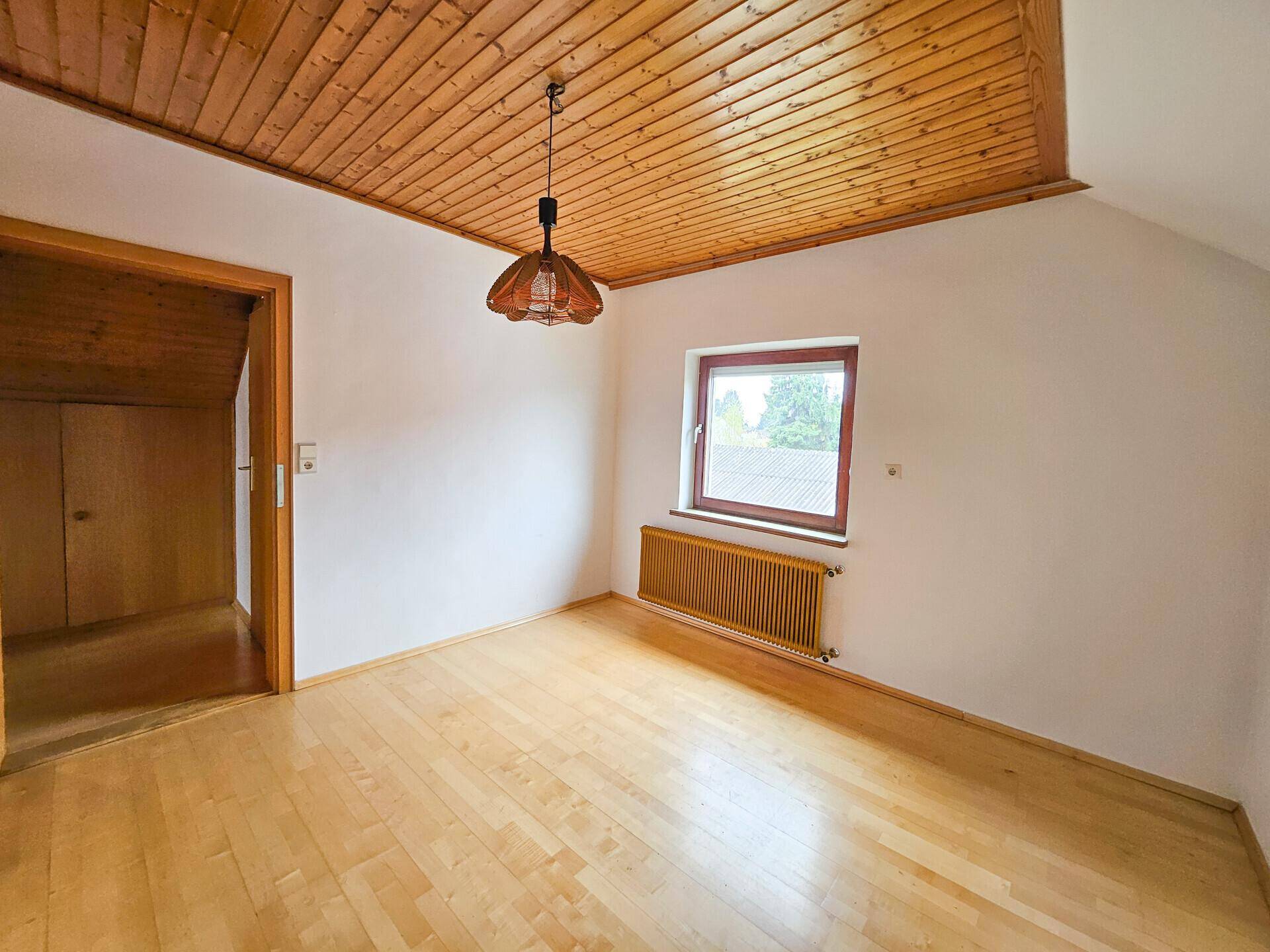 Gemütliches Zimmer mit Holzbalkendecke, Parkettboden und Fenster.