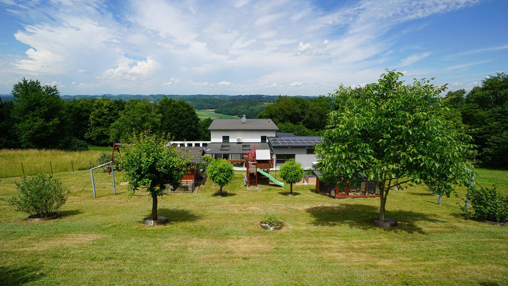 Panoramablick auf das moderne Wohnhaus mit weitläufigem Garten und Spielplatz in ländlicher Umgebung.