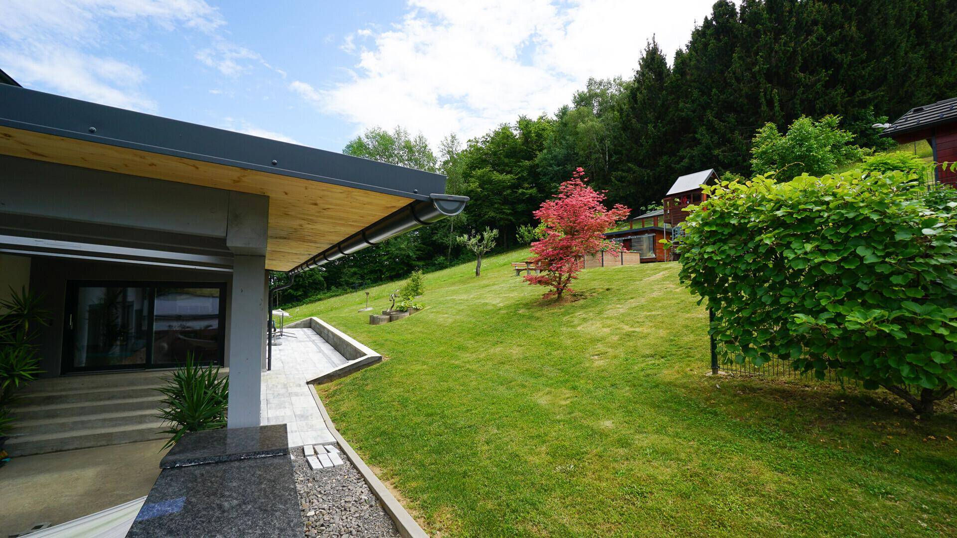 Überdachte Terrasse mit Zugang zum Haus und Blick auf den weitläufigen, grünen Garten.