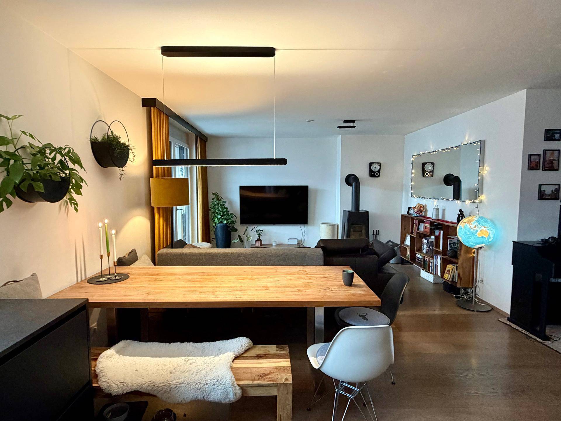 Offener Wohn- und Essbereich mit Holztisch, Kaminofen und gemütlicher Sitzecke, hell und modern.