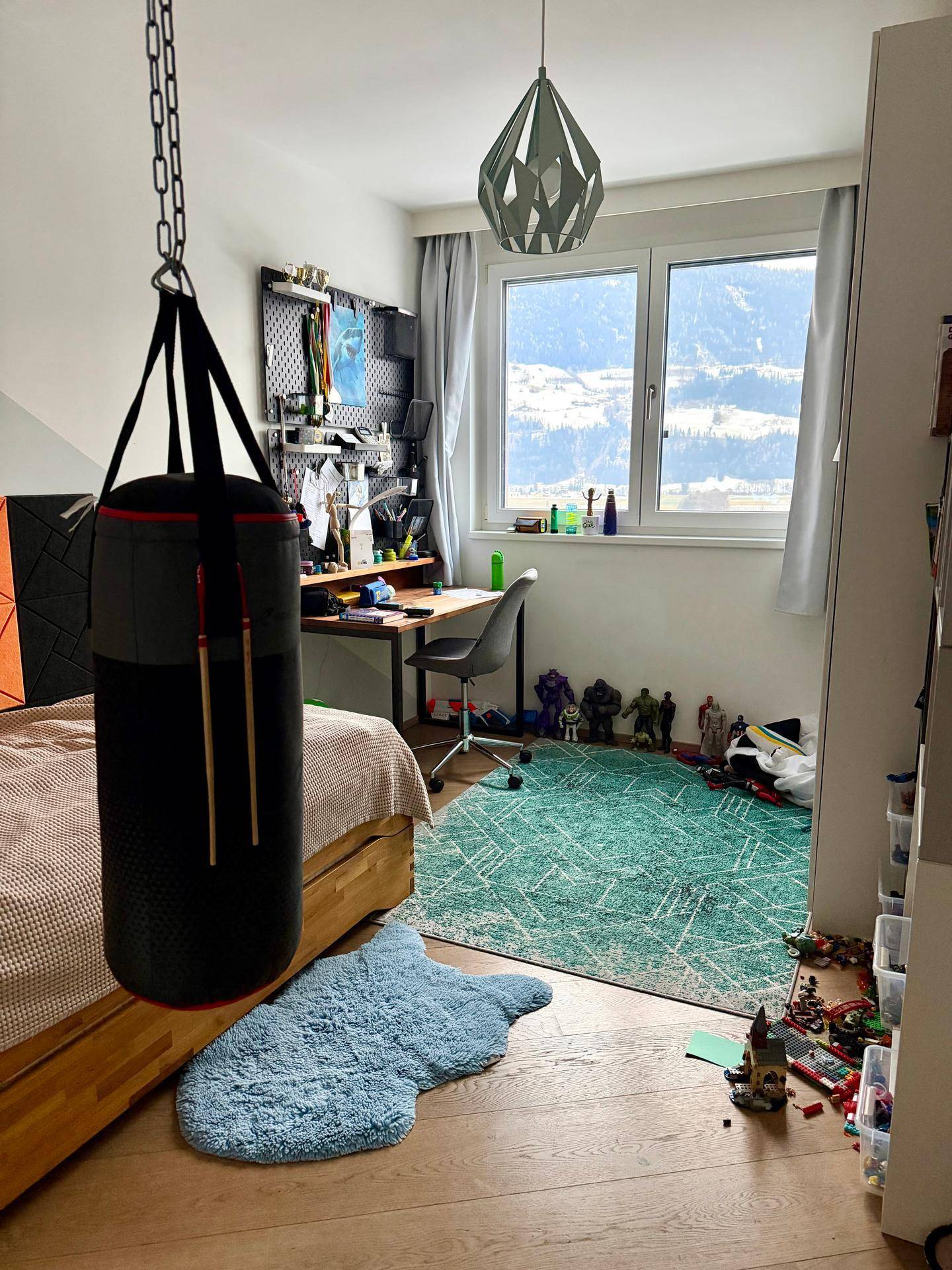 Kinderzimmer mit Schreibtisch, Holzfußboden und einem Boxsack, bietet einen weiten Blick auf die Berge.