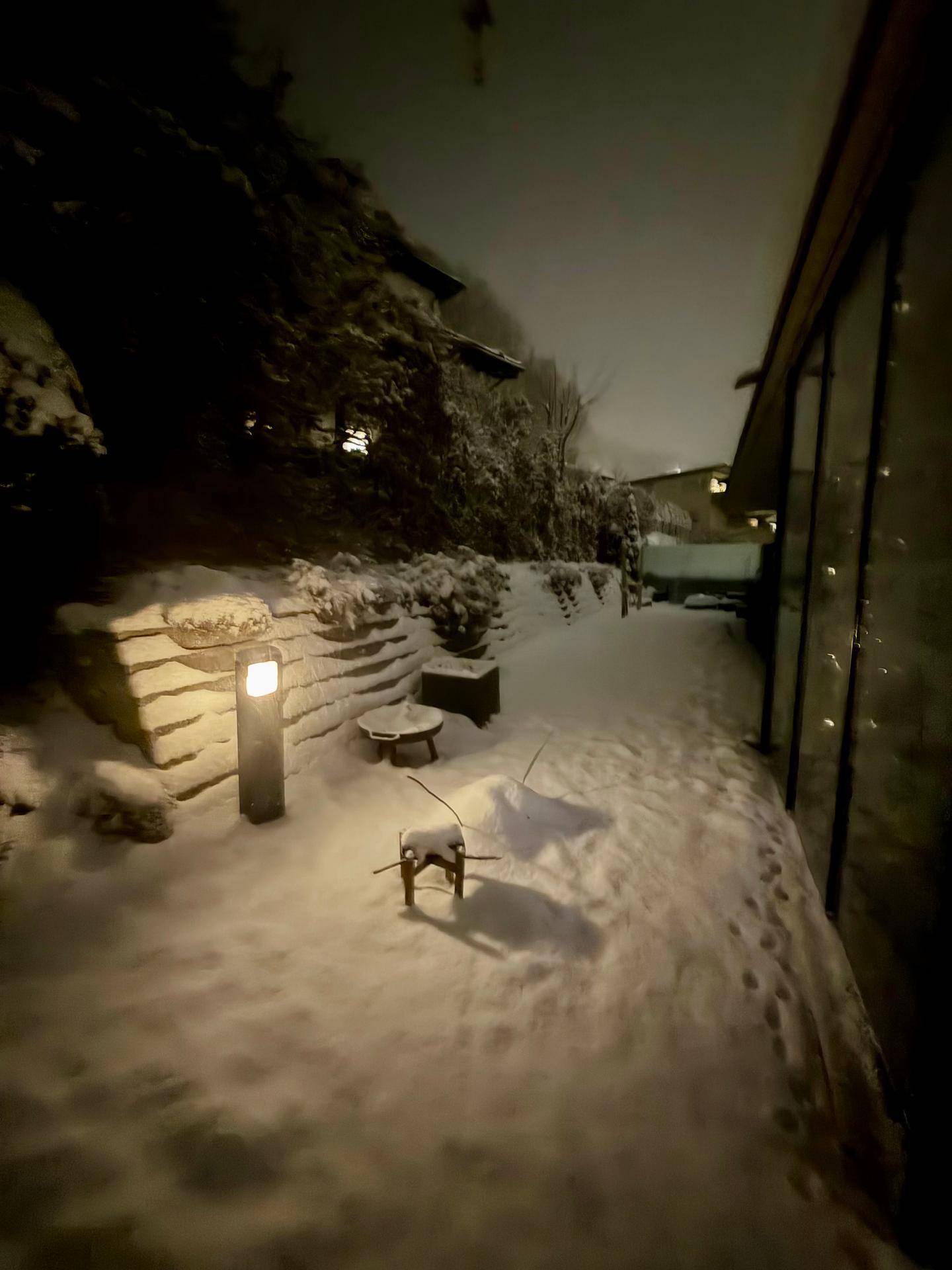 Verschneiter Außenbereich bei Nacht mit Beleuchtung und winterlicher Atmosphäre.