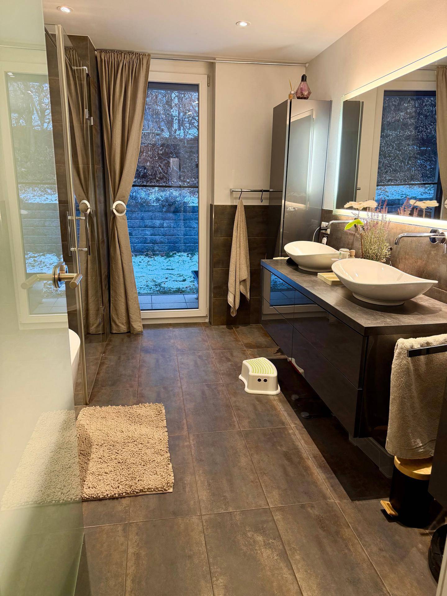 Modernes Badezimmer mit Doppelwaschbecken, großer Dusche und Zugang zum Außenbereich.