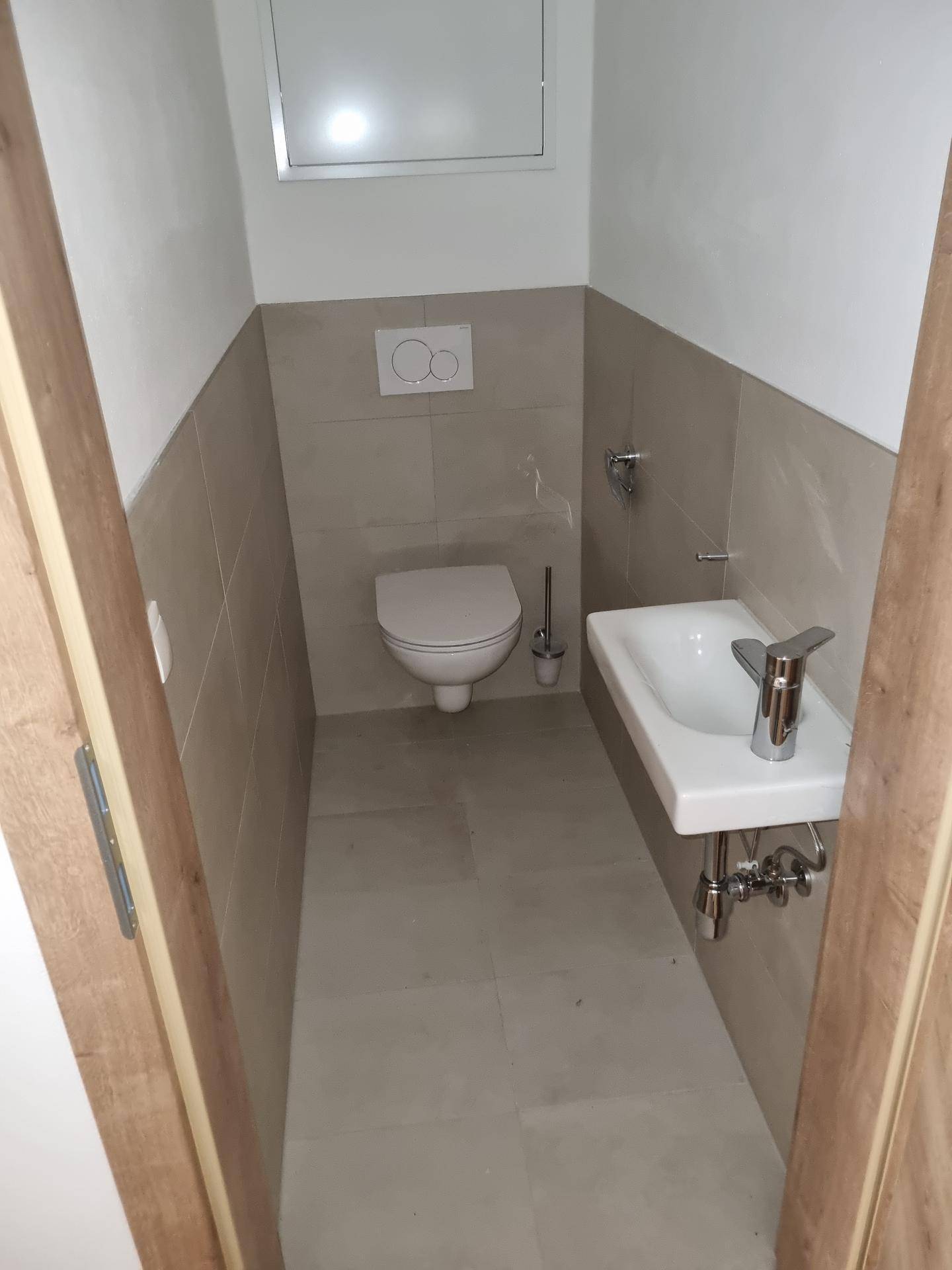 Helles Gäste-WC mit wandhängender Toilette, kleinem Waschbecken und modernen Fliesen.