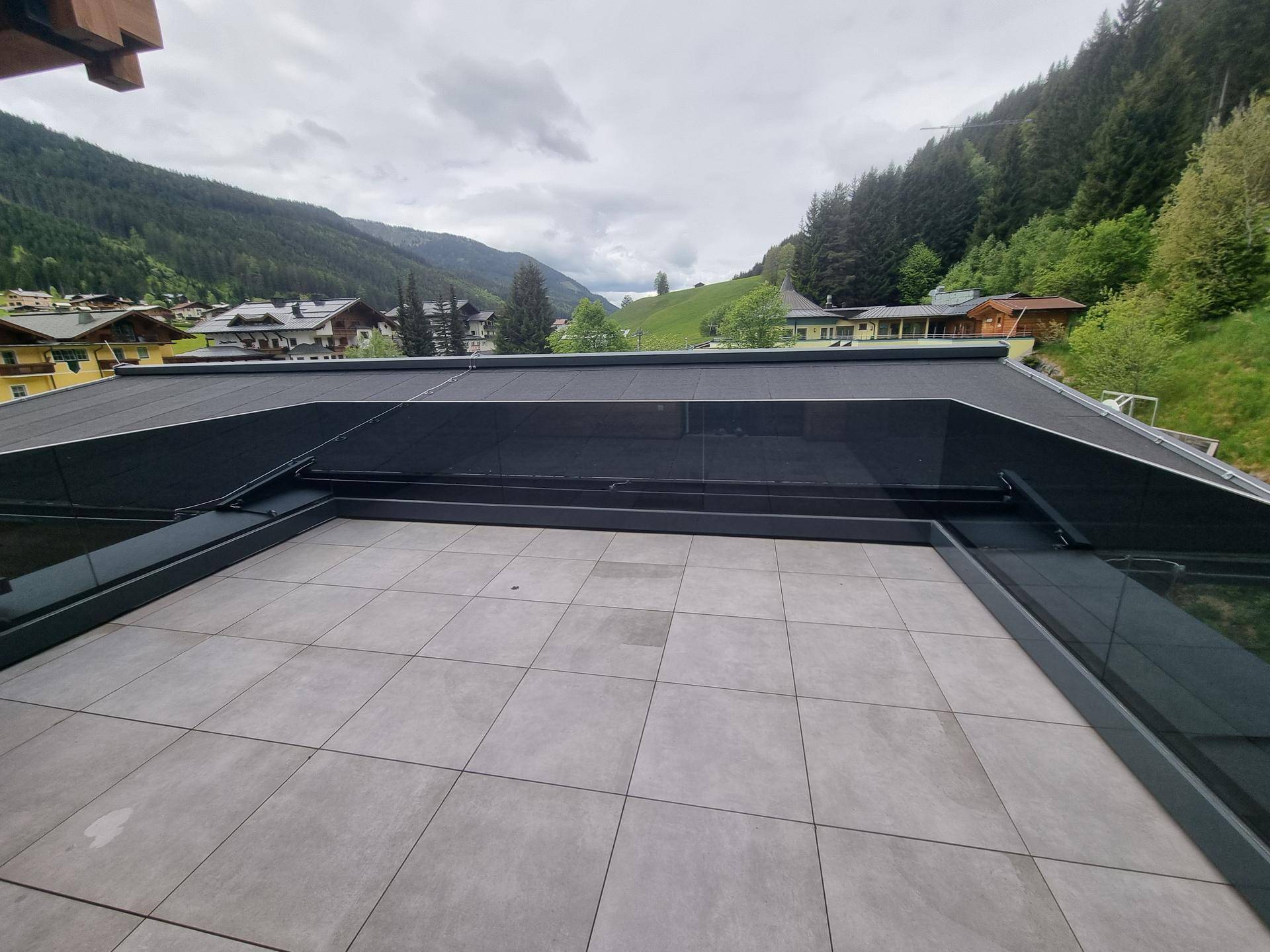 Große, geflieste Terrasse mit Glasgeländer und weitem Blick auf die Berge und das Tal.