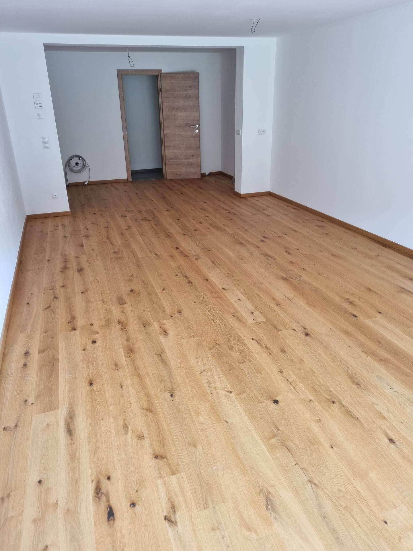 Geräumiger, heller Wohnraum mit Holzboden und Holztür, bereit zur individuellen Gestaltung.