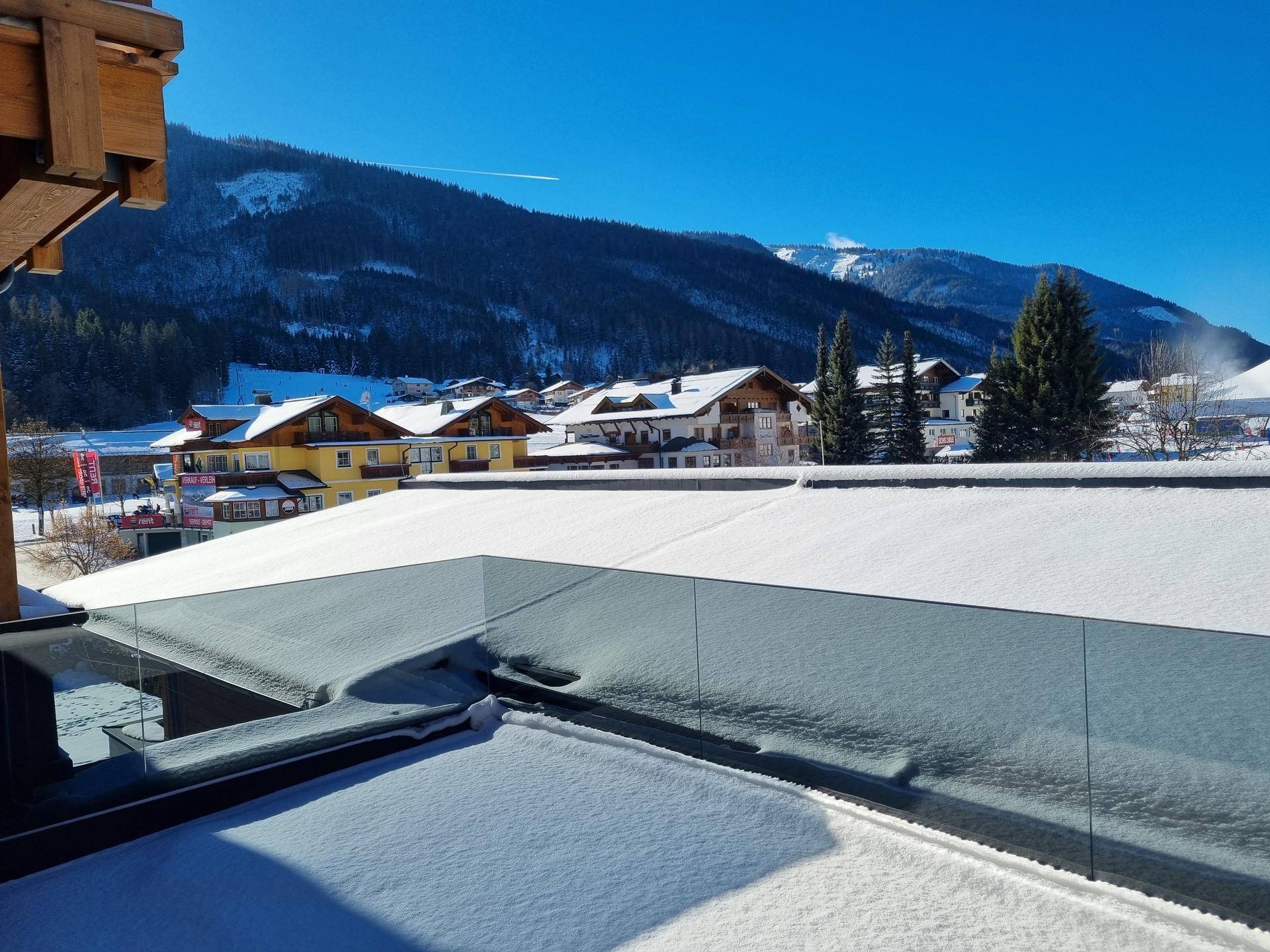Sonniger Wintertag auf der Terrasse mit weitem Blick über die verschneite Alpenlandschaft.