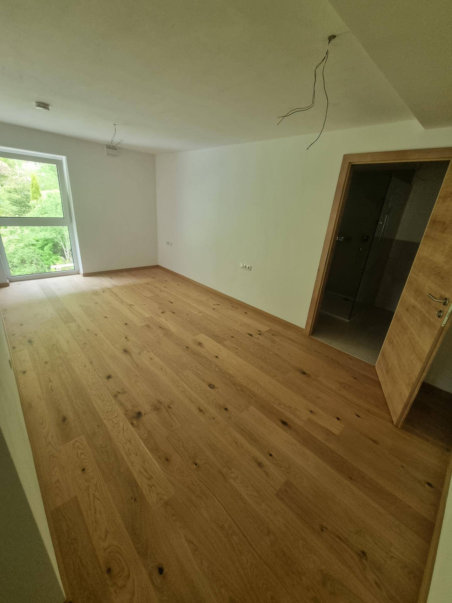 Lichtdurchflutetes Zimmer mit Holzboden und Fenster mit Blick auf die umliegende Natur.