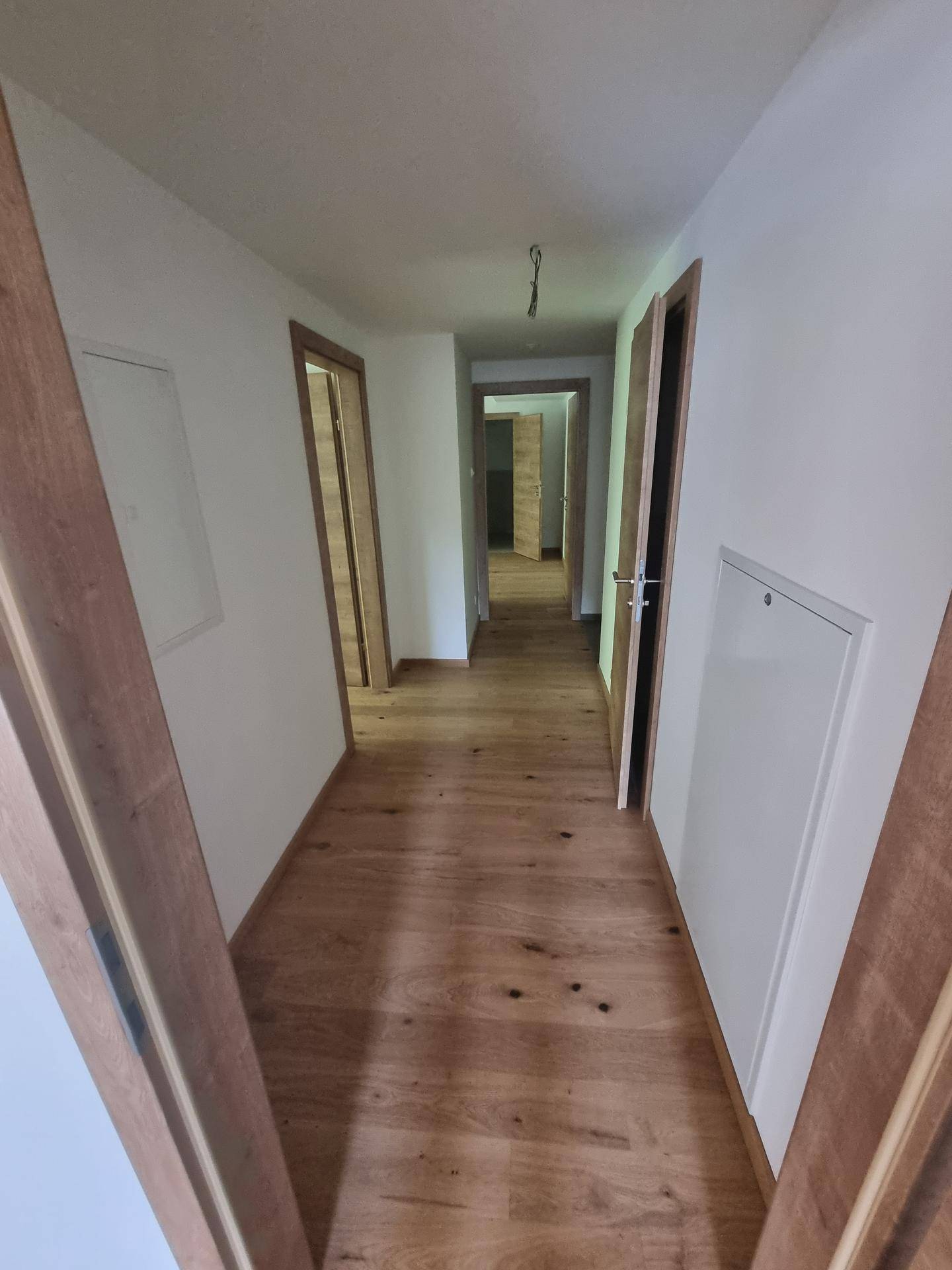Heller Flur mit Holzboden und mehreren Türen, der verschiedene Räume miteinander verbindet.