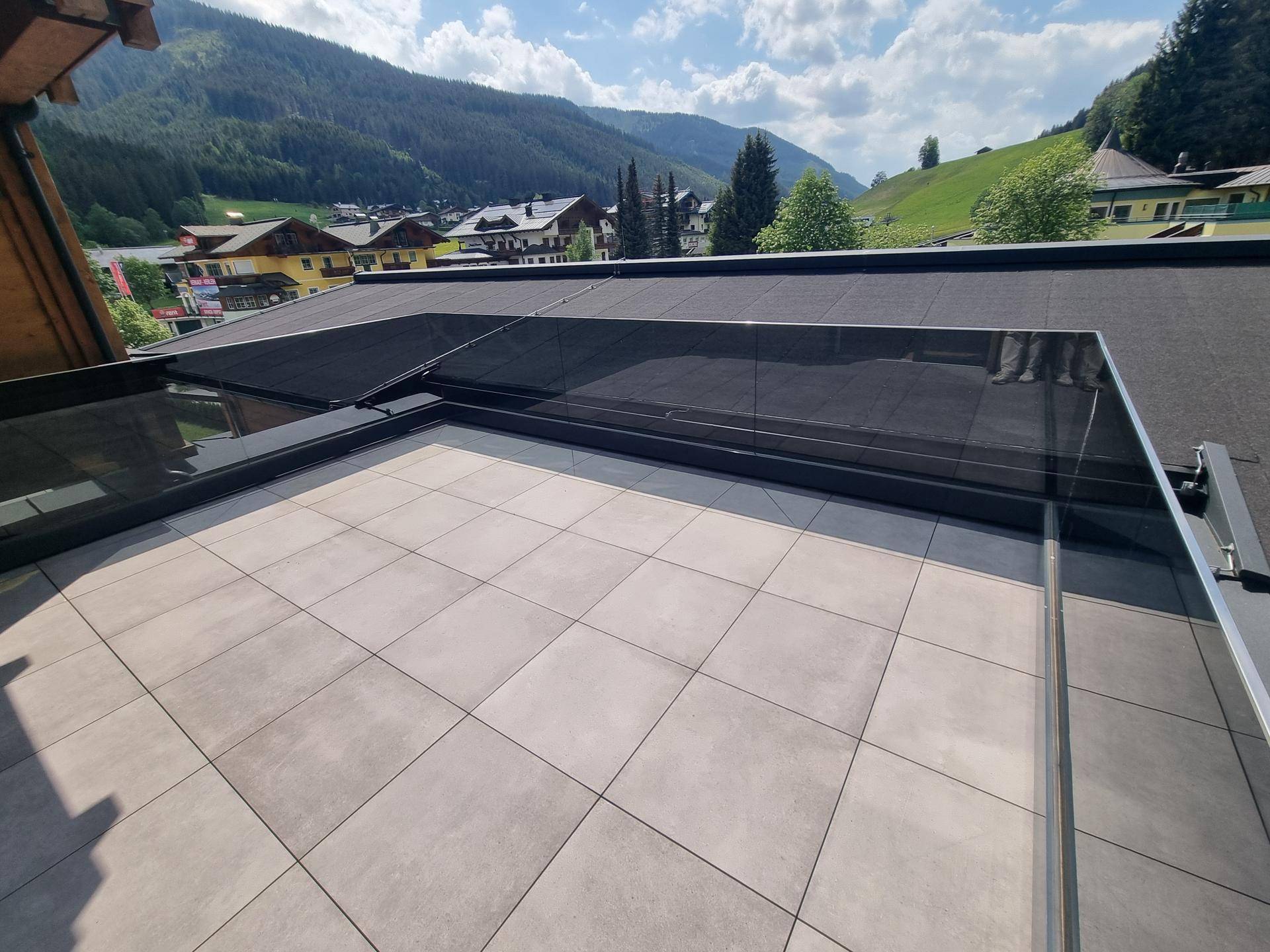 Sonnenterrasse mit Fliesenboden und beeindruckendem Ausblick auf die umliegenden Berge und Wälder.