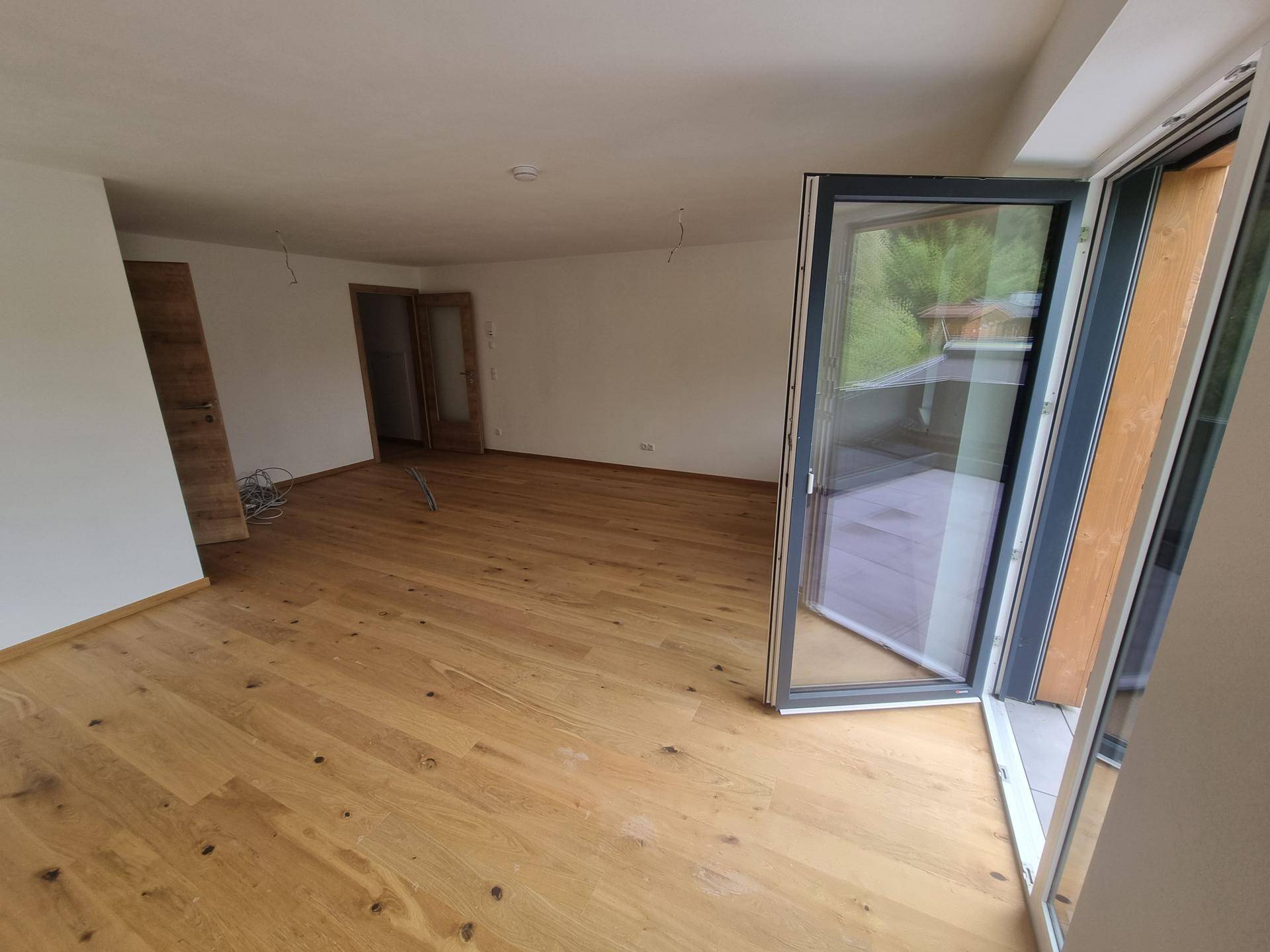 Geräumiges, helles Zimmer mit Holzboden und Blick ins Grüne, bereit für die Einrichtung.