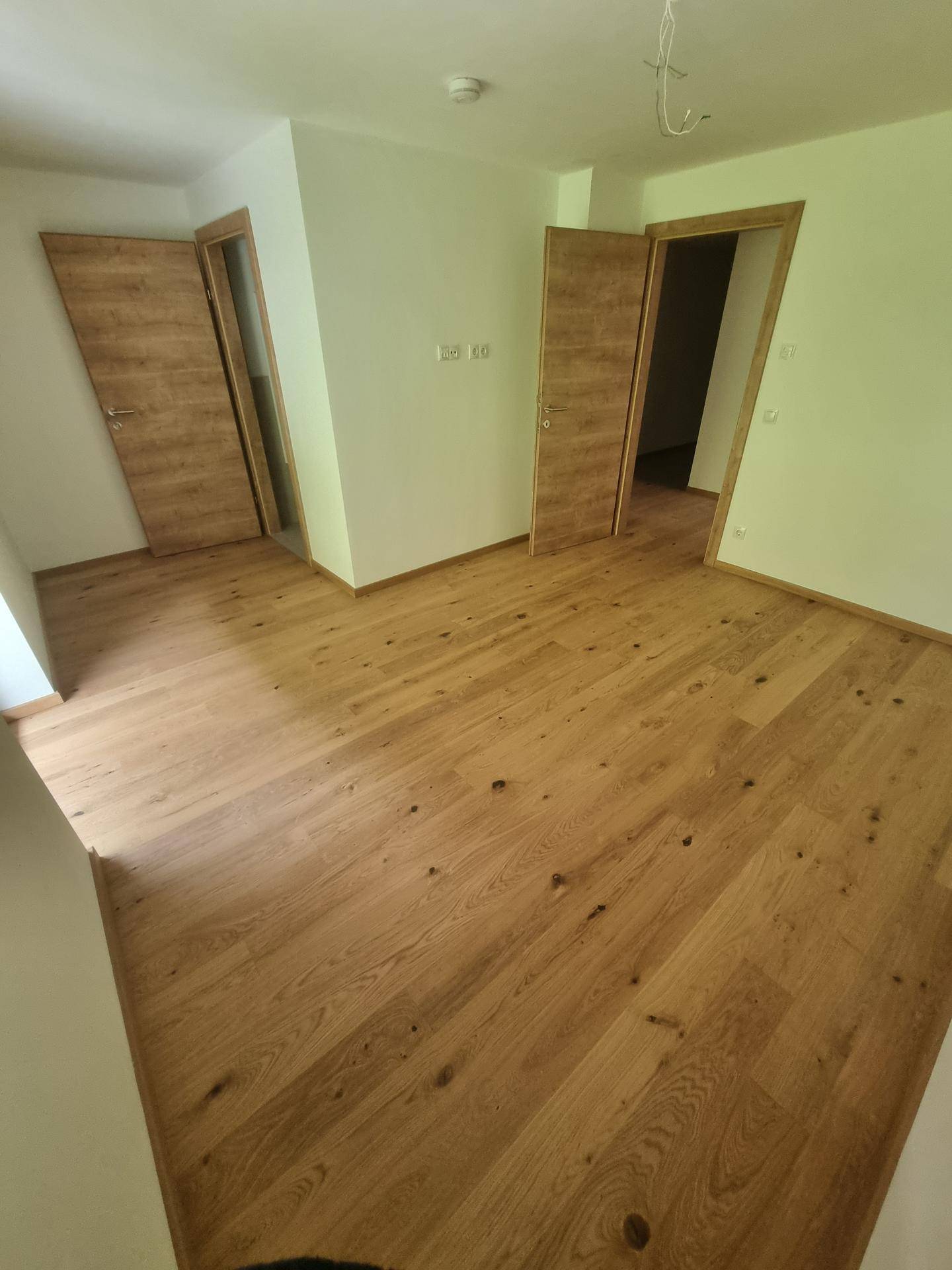 Leeres Zimmer mit Holzboden und mehreren Holztüren, bereit zur individuellen Gestaltung.