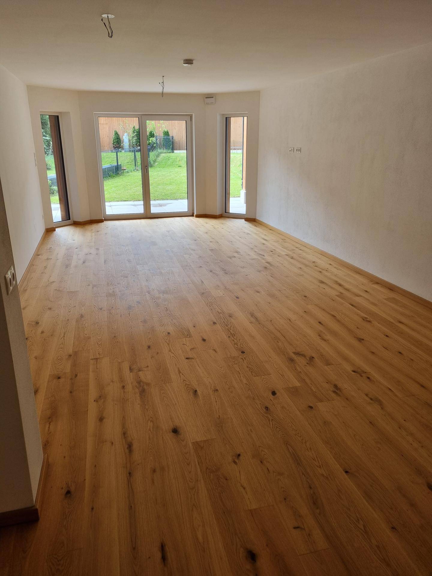 Heller, unmöblierter Wohnraum mit Eichenparkett und großen Fenstern zum Garten.
