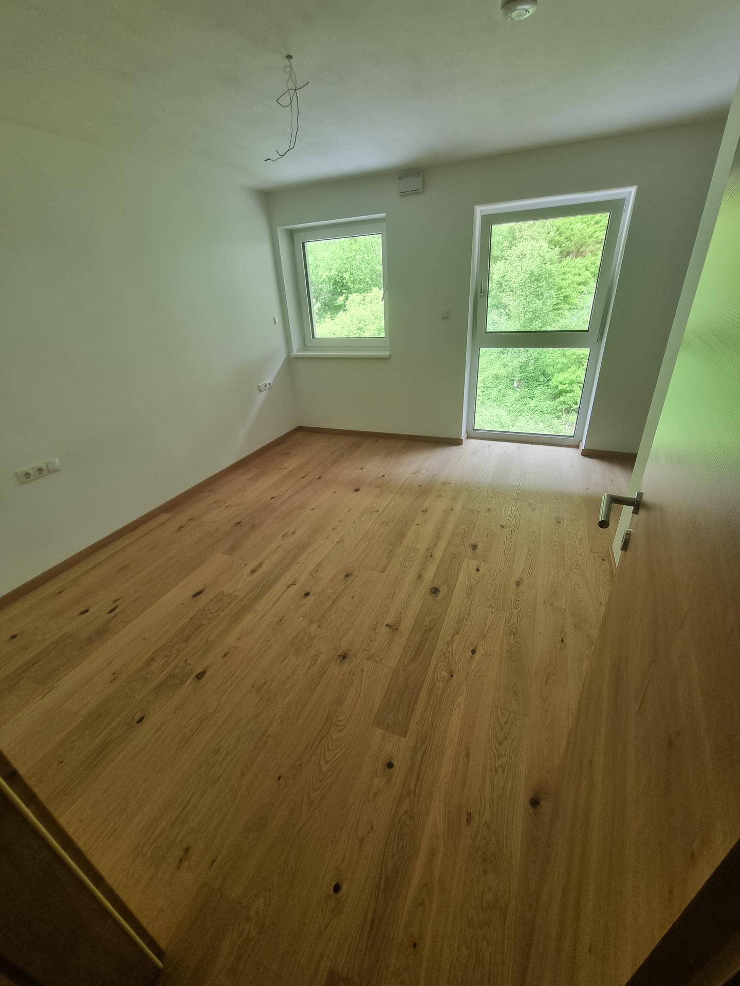 Helles Schlafzimmer mit Holzboden und großen Fenstern, die einen Blick ins Grüne bieten.