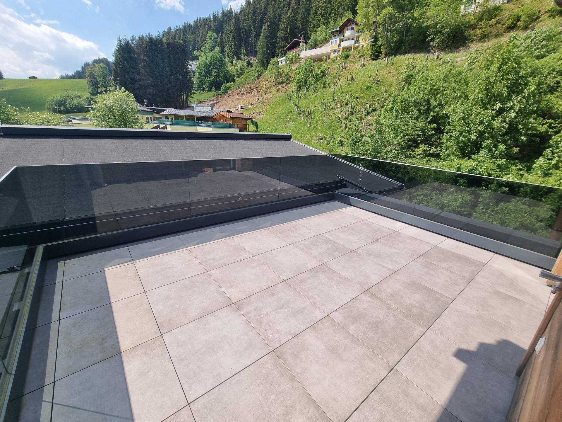 Geräumige Terrasse mit modernen Fliesen und Panoramablick auf die grüne Bergwelt.