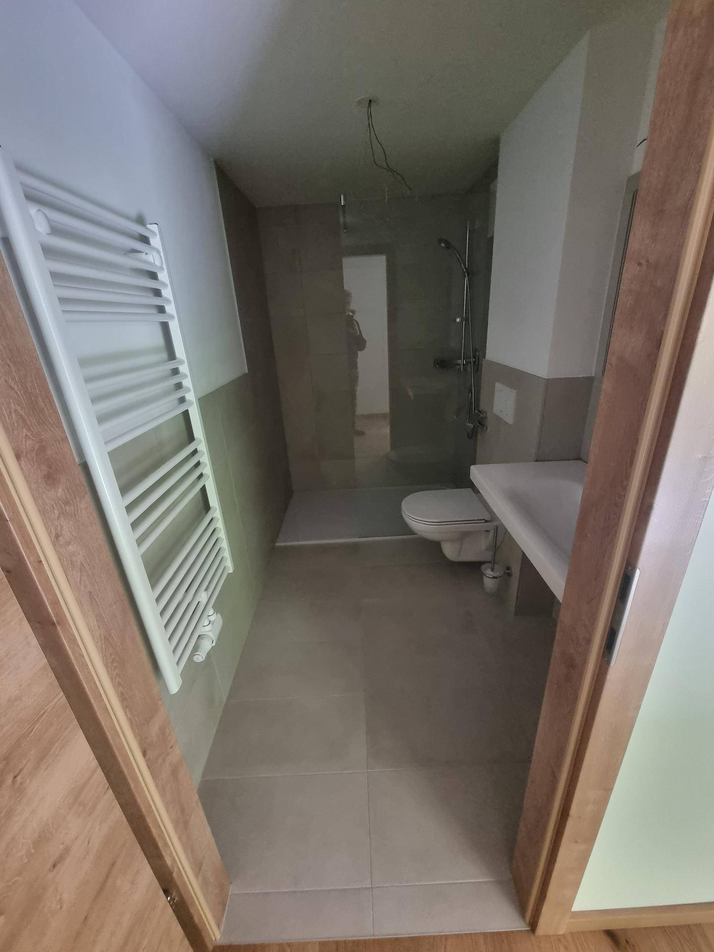 Modernes Badezimmer mit ebenerdiger Dusche, WC, Waschbecken und Handtuchheizkörper.