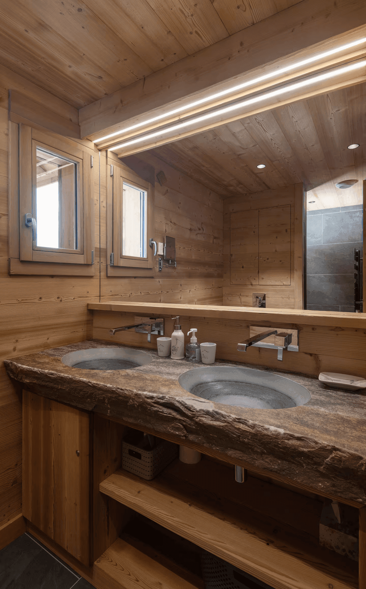 Modernes Badezimmer mit Doppelwaschbecken aus Naturstein und Holzwänden im alpinen Stil.
