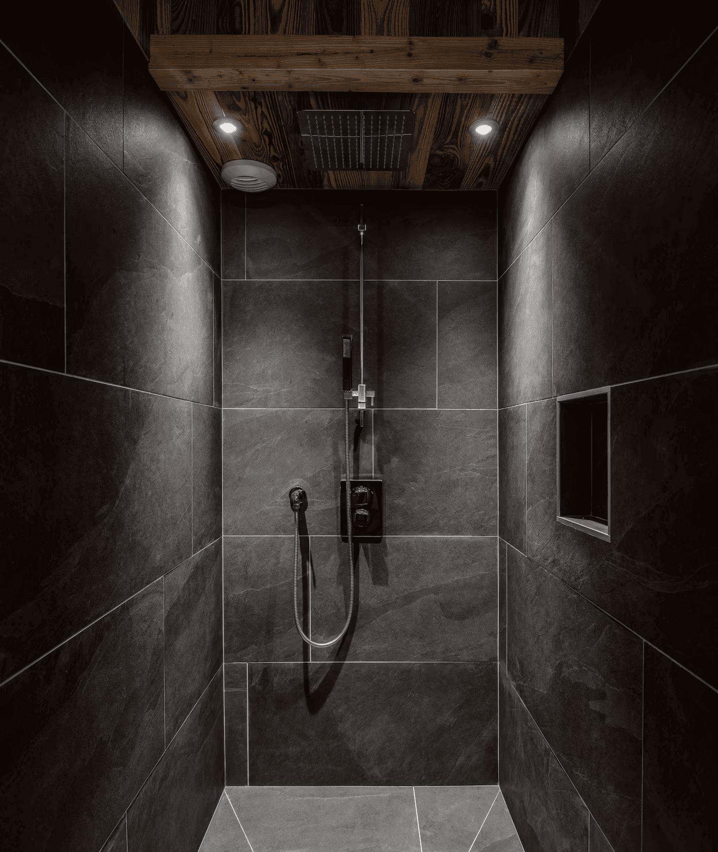 Moderne Duschkabine mit dunklen Fliesen, Regendusche und integrierter Beleuchtung.