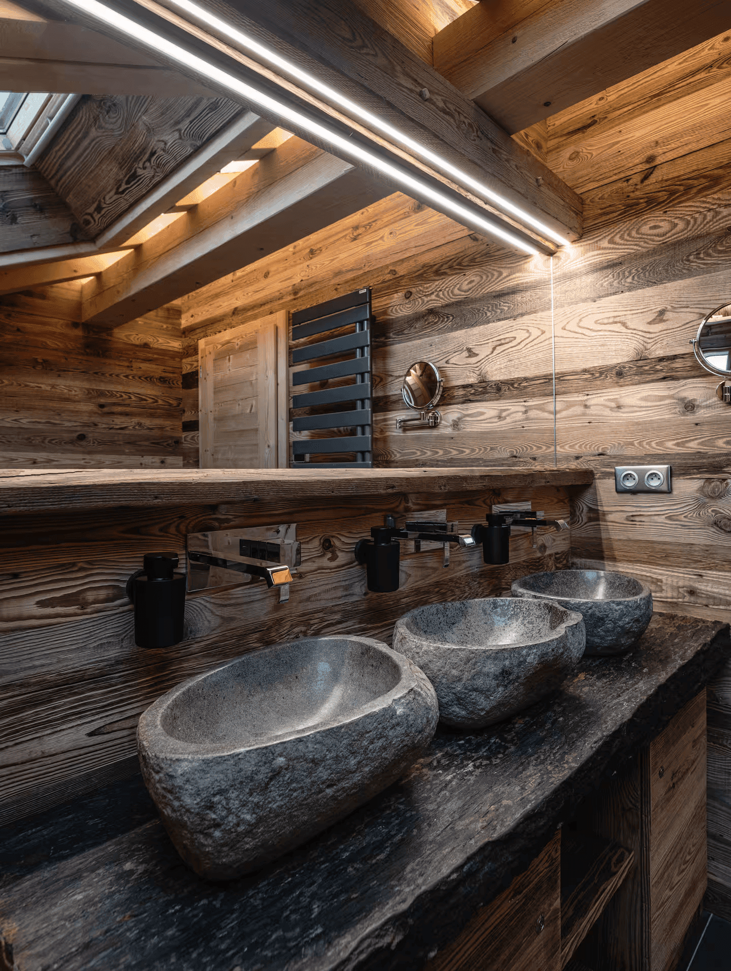 Detailansicht der Natursteinwaschbecken in einem luxuriösen Badezimmer mit Holzwänden und Spiegel.