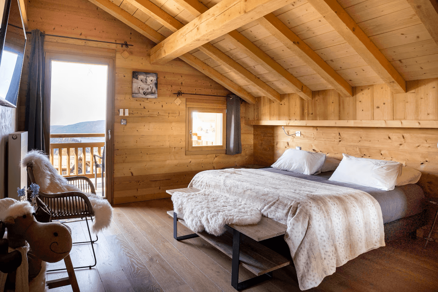 Gemütliches Schlafzimmer im Dachgeschoss mit Holzwänden, Holzbalkendecke und Balkonzugang.