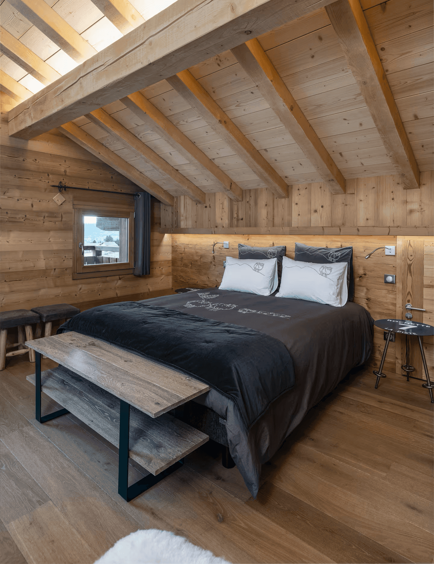 Komfortables Schlafzimmer im Dachgeschoss mit Holzwänden, Holzbalkendecke und indirekter Beleuchtung.