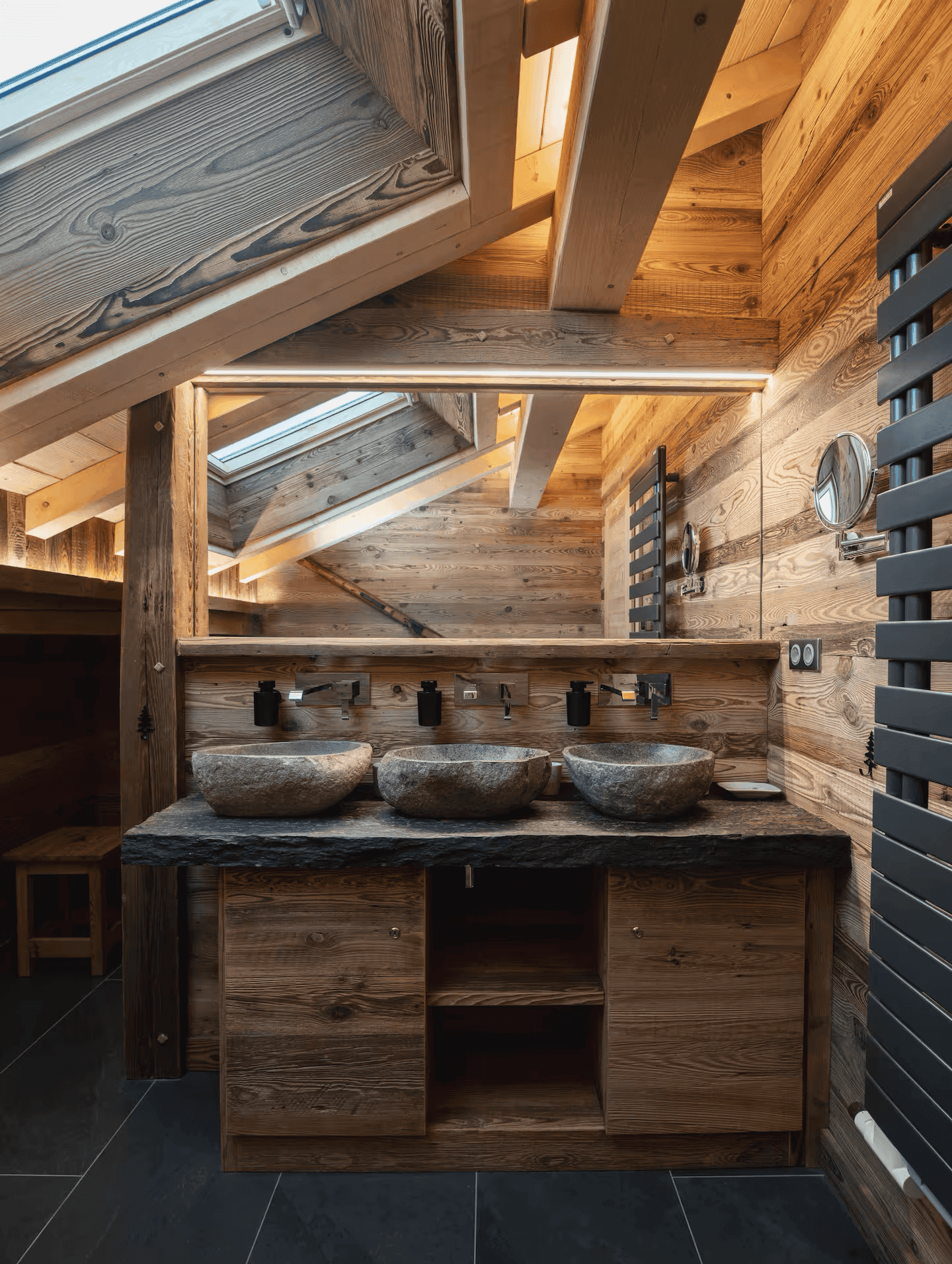 Luxuriöses Badezimmer mit drei Natursteinwaschbecken, Holzwänden und Dachfenster für viel Licht.