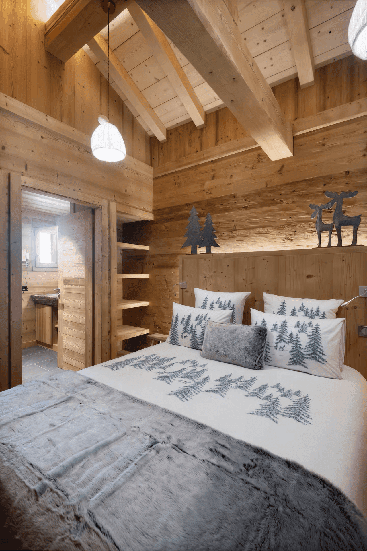 Rustikales Schlafzimmer mit Holzwänden, Holzbalkendecke und Zugang zu einem angrenzenden Bad.