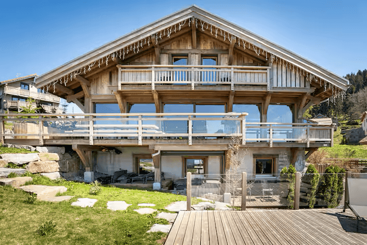 Charmantes Holzchalet mit großer Fensterfront, Balkonen und einer kleinen Rasenfläche im Vordergrund.