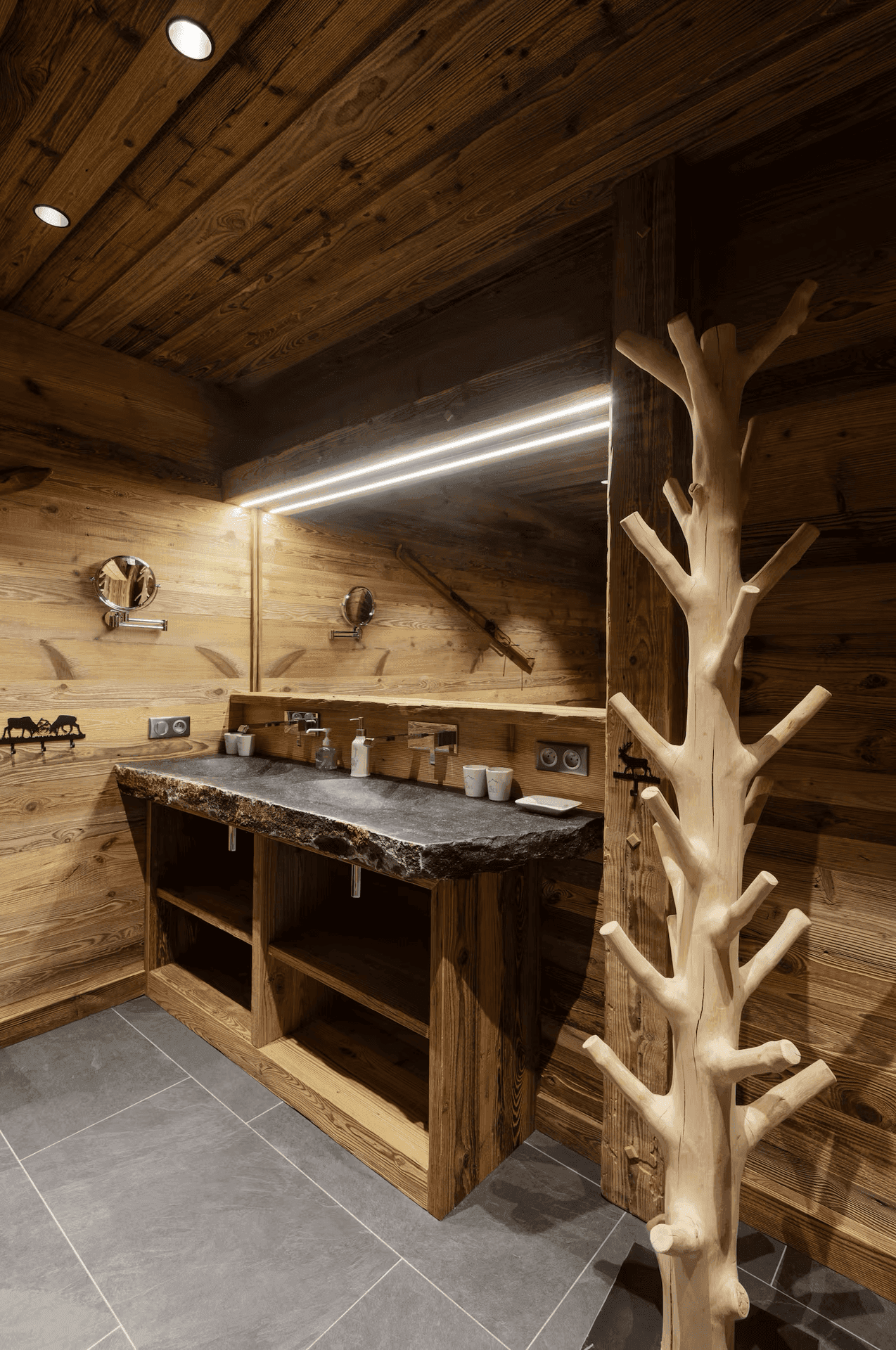 Elegantes Badezimmer mit Natursteinwaschbecken, Holzwänden und großem Spiegel mit Beleuchtung.