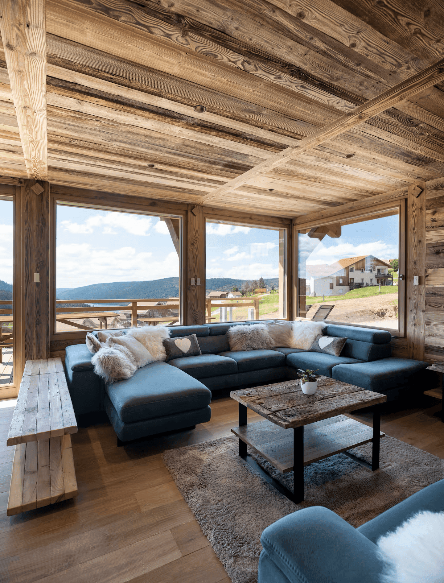 Helles Wohnzimmer mit großem Ecksofa, Holzboden und Panoramafenstern mit Bergblick.