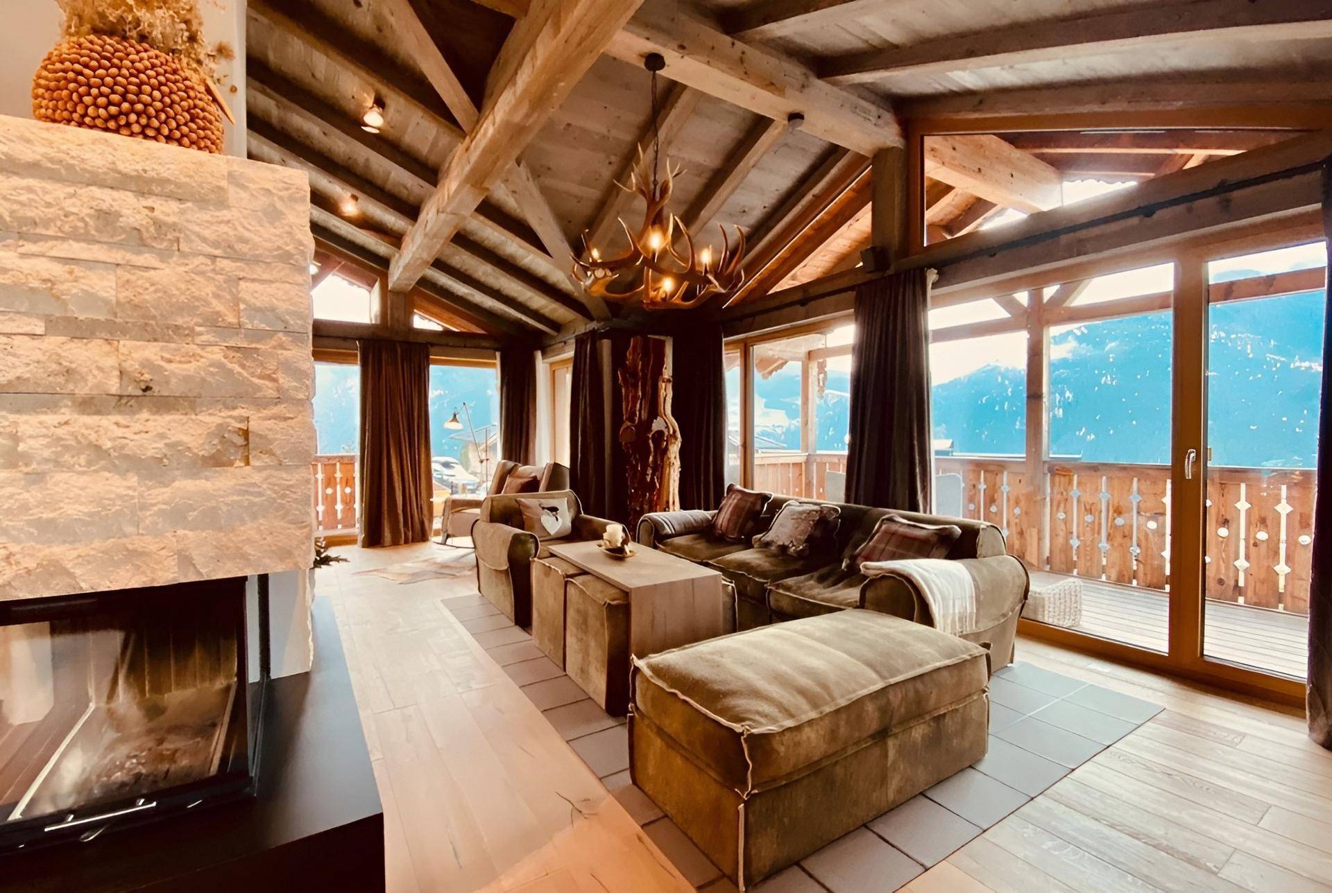 Gemütliches Wohnzimmer mit Holzbalkendecke, Kamin und Panoramafenstern mit Bergblick.