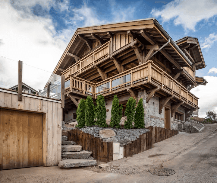 Rustikales Holzchalet mit Steinfundament und mehreren Balkonen, umgeben von alpiner Landschaft.