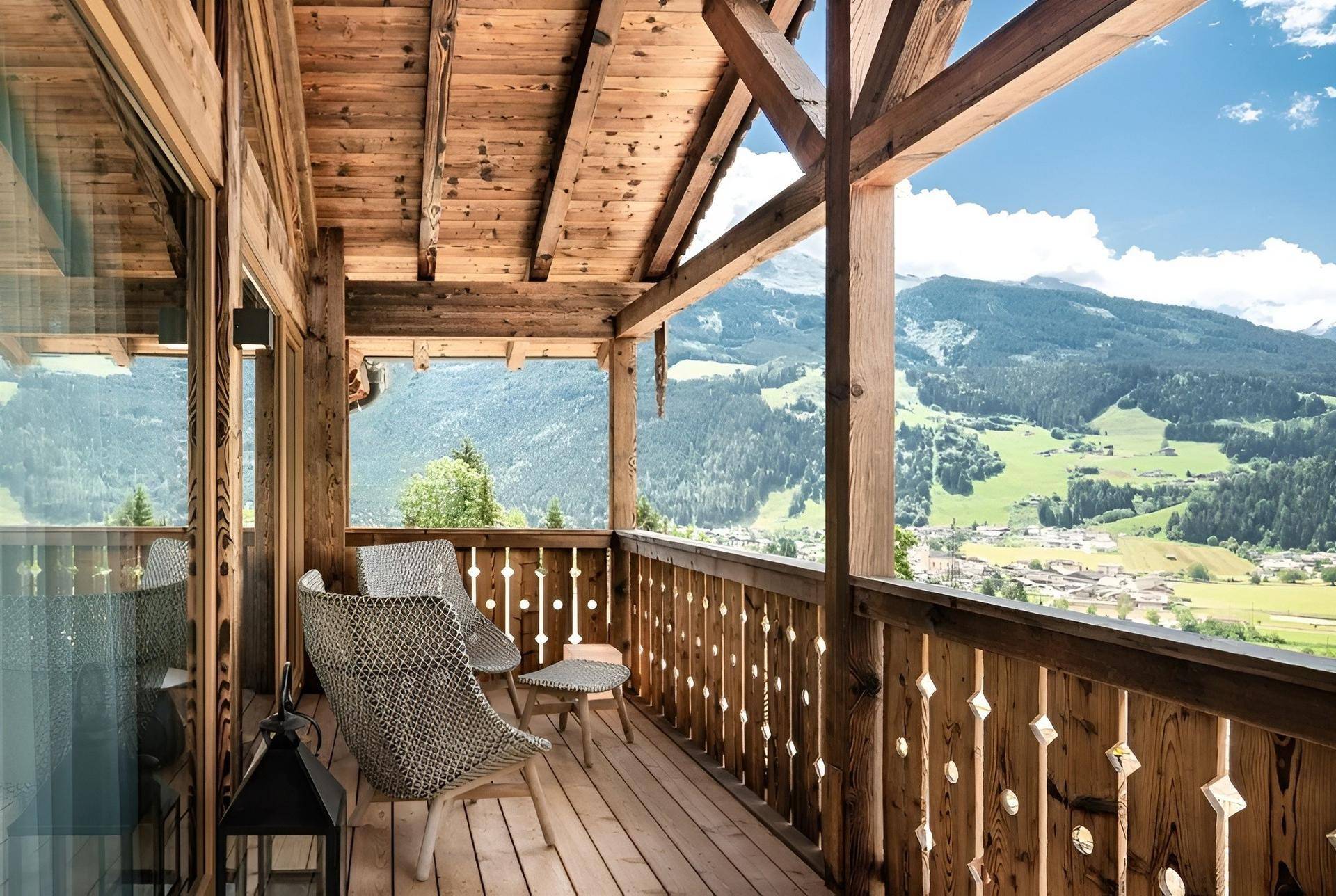 Geräumiger Holzbalkon mit Sitzgelegenheiten und weitem Blick über das grüne Tal und die Berge.