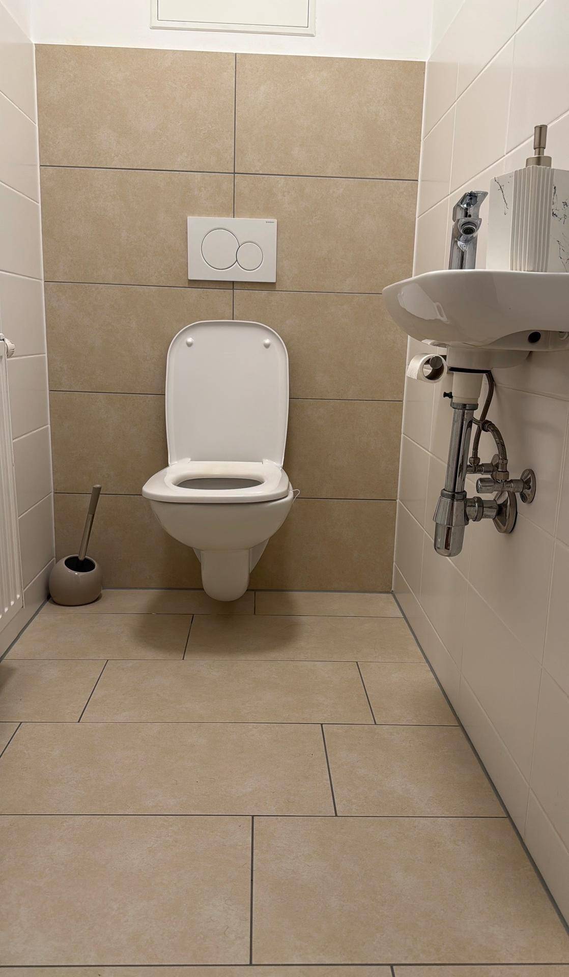 Modernes Gäste-WC mit wandhängender Toilette, kleinem Waschbecken und beigefarbenen Fliesen.